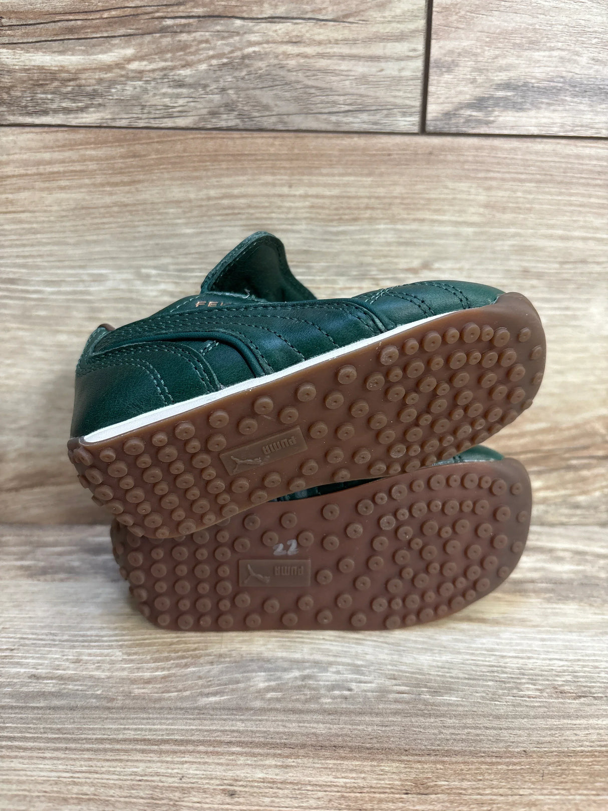 Bottom and side view of Puma x Fenty Avanti L toddler sneakers in dark myrtle with brown studded rubber soles, velcro strap, size 22 on wood floor