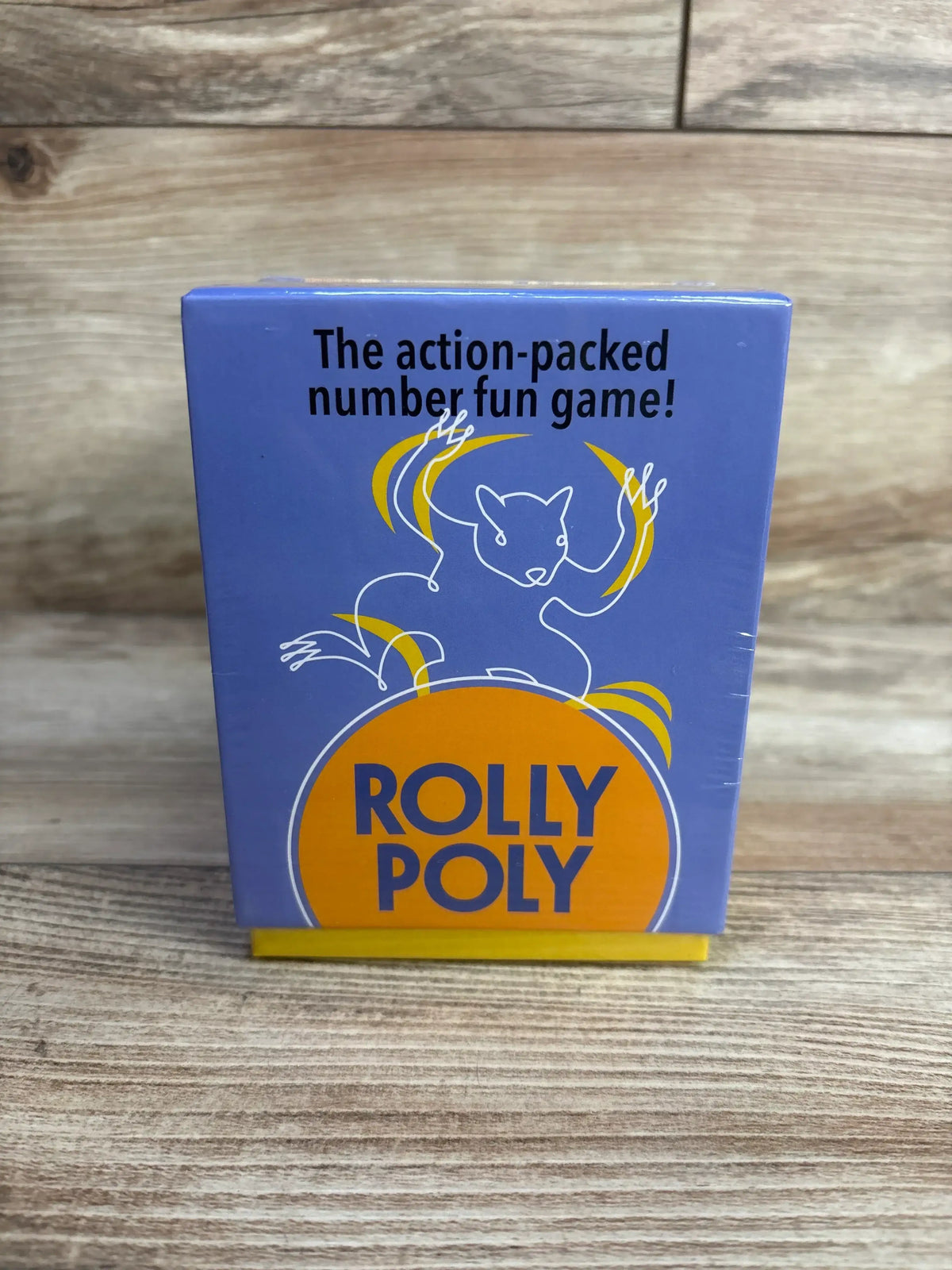 Front of Rolly Poly game box, purple with orange ROLLY POLY and headline The action-packed number fun game on wood tabletop
