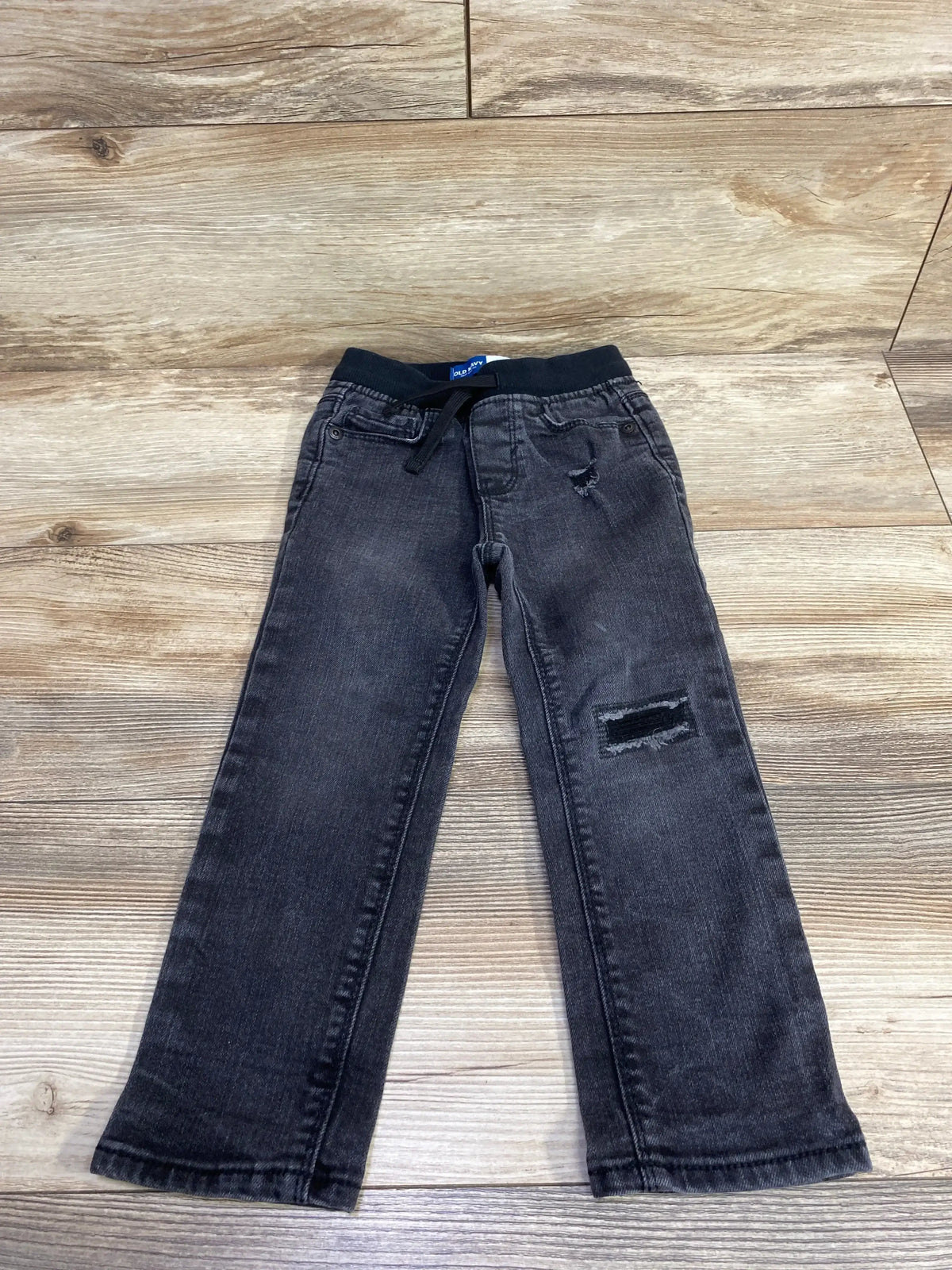 Flat lay of Old Navy karate skinny jeans in black size 3T showcasing elastic waistband, patch detail and front pockets on wood floor