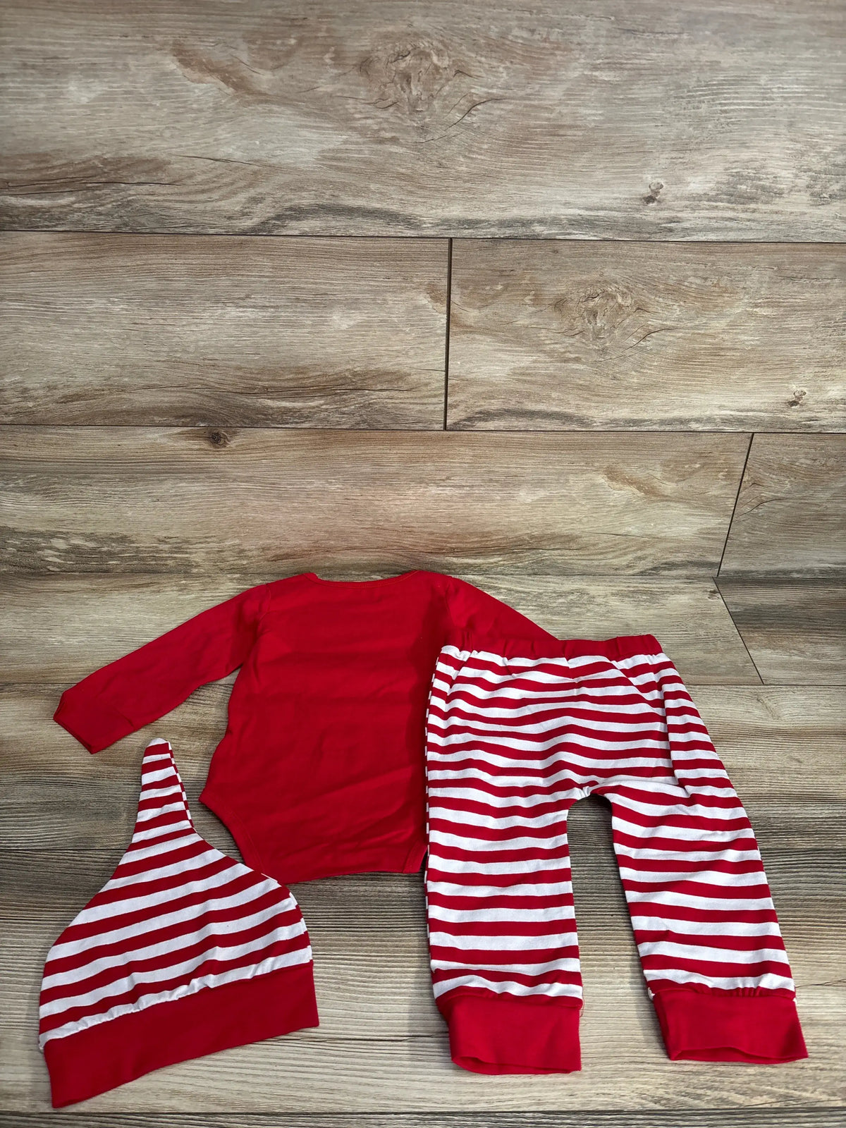 Red baby onesie with striped pants and hat, holiday-themed kids clothing set on wood floor