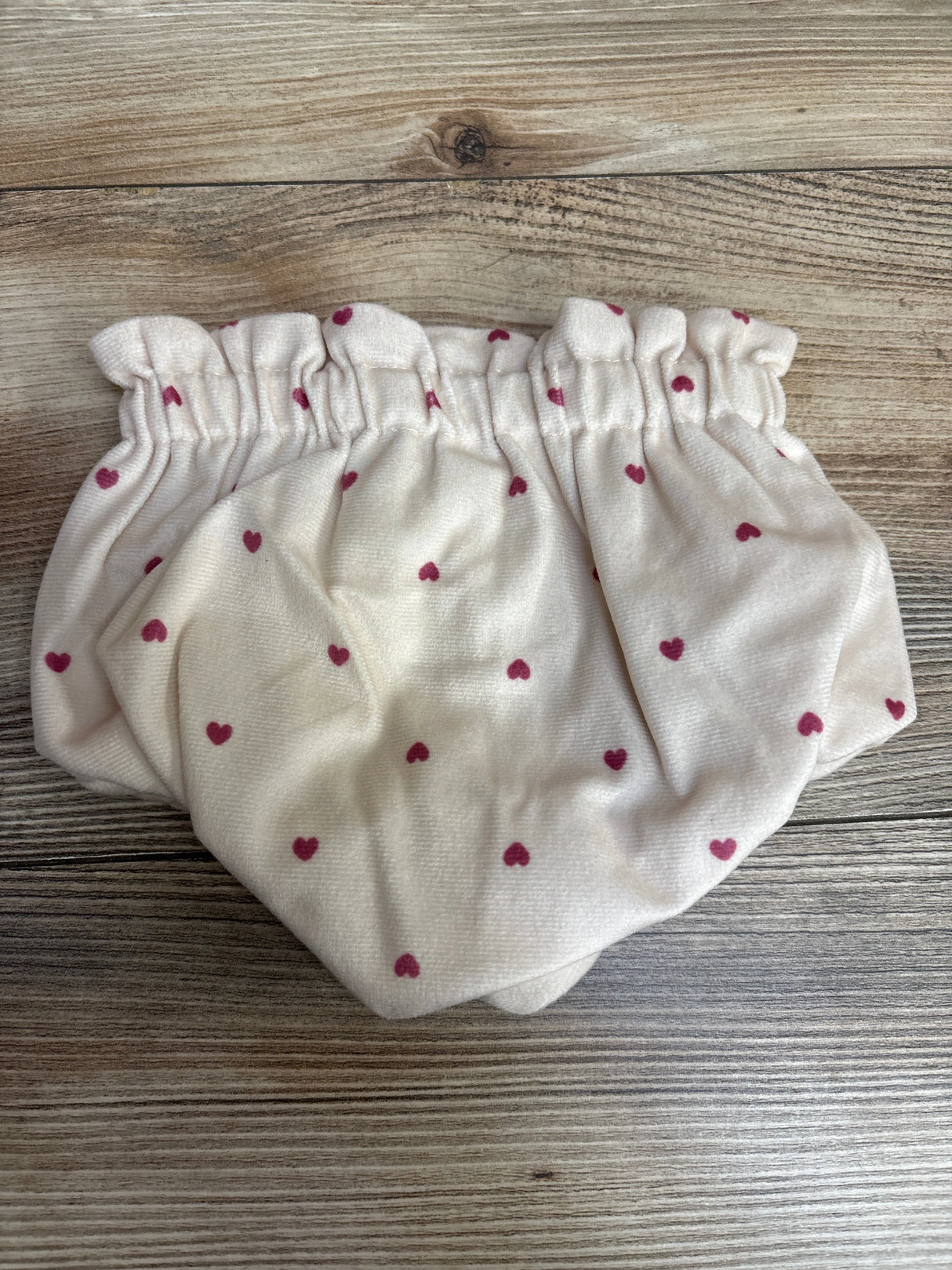 Soft white baby bloomers with red heart print on wooden surface