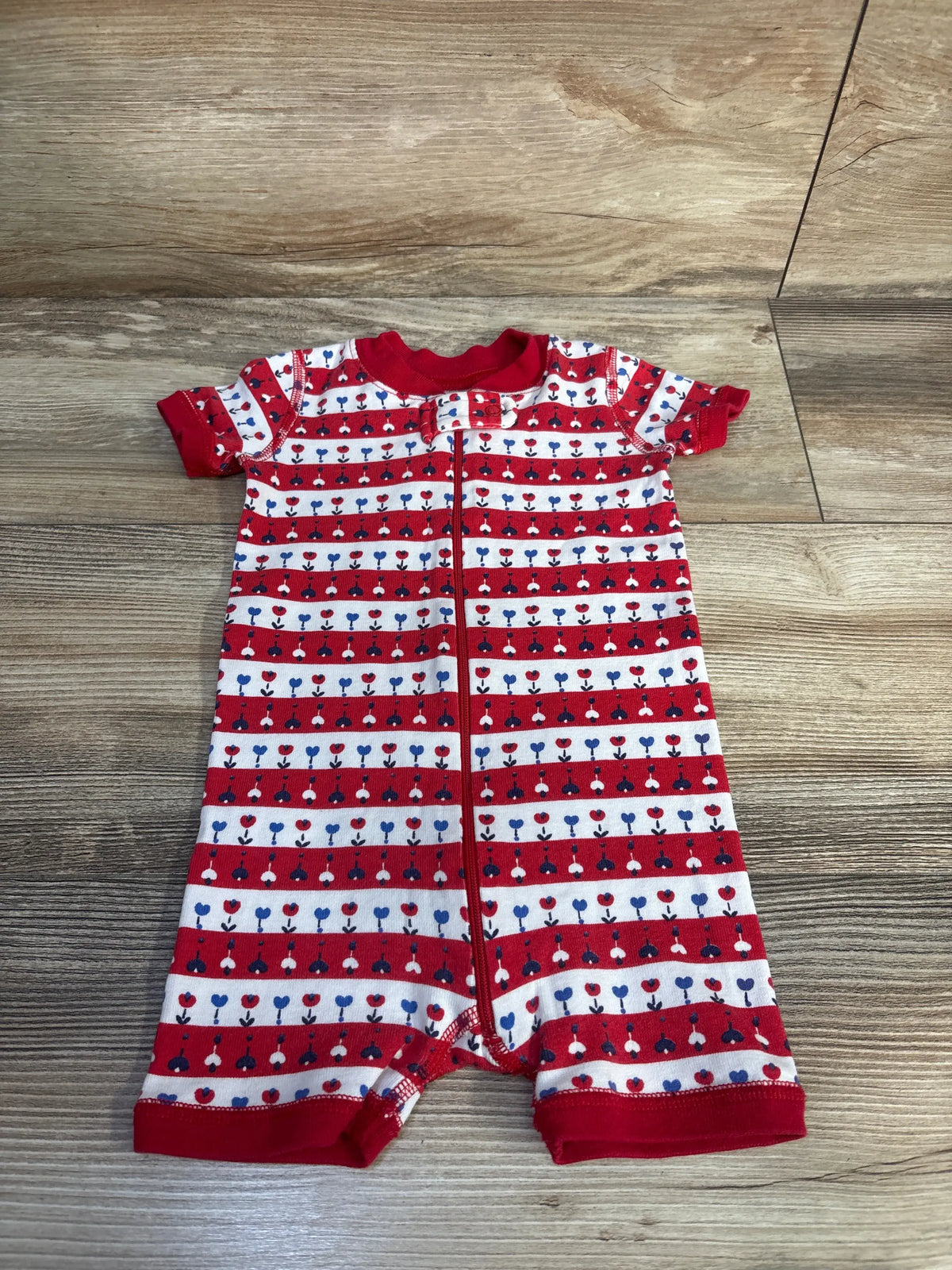 Front view of red Hanna Andersson Fourth of July romper sleeper showcasing patriotic floral pattern and front zipper on wood flooring