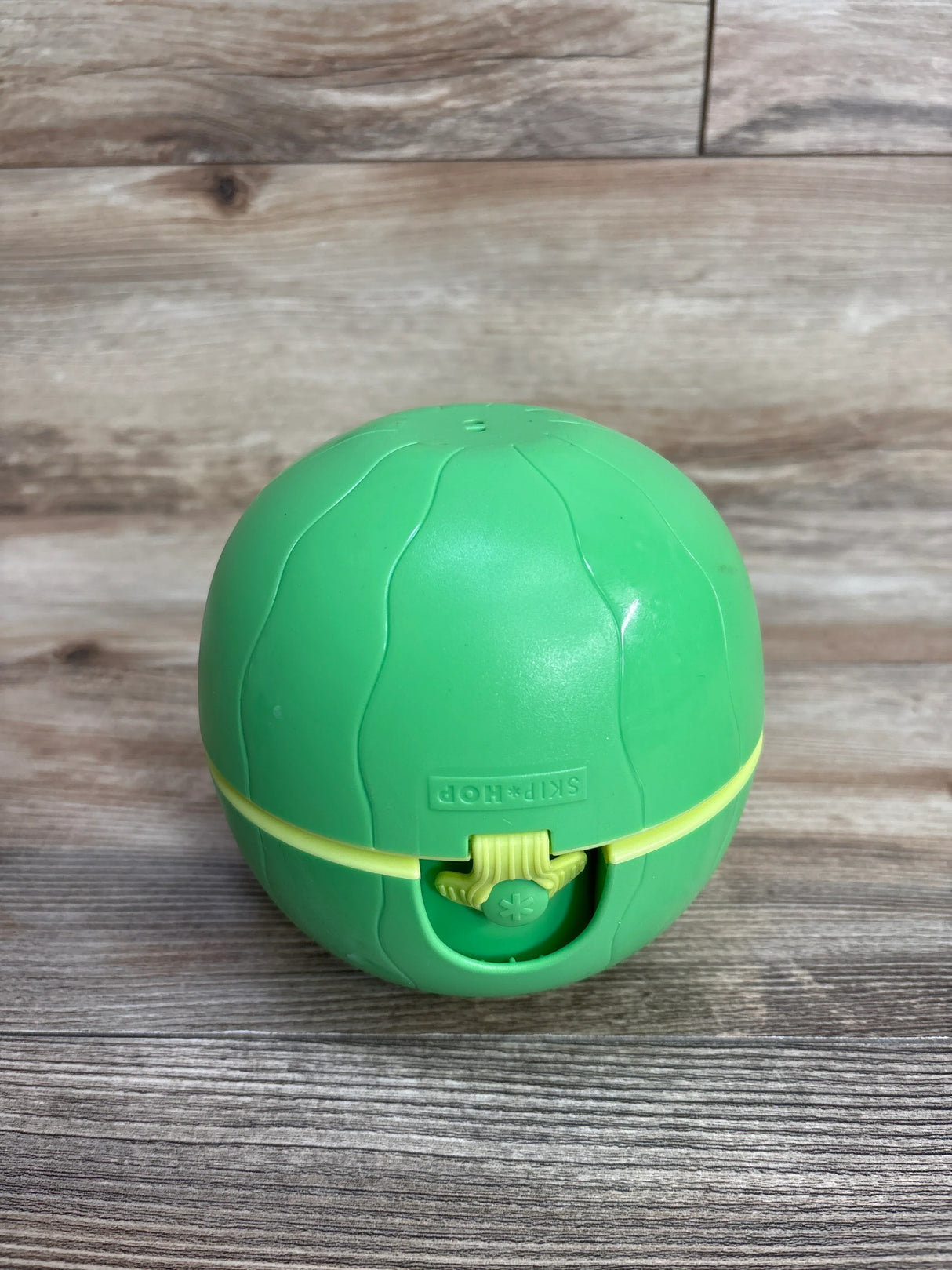 Green Skip Hop ball toy with textured lines on wooden surface