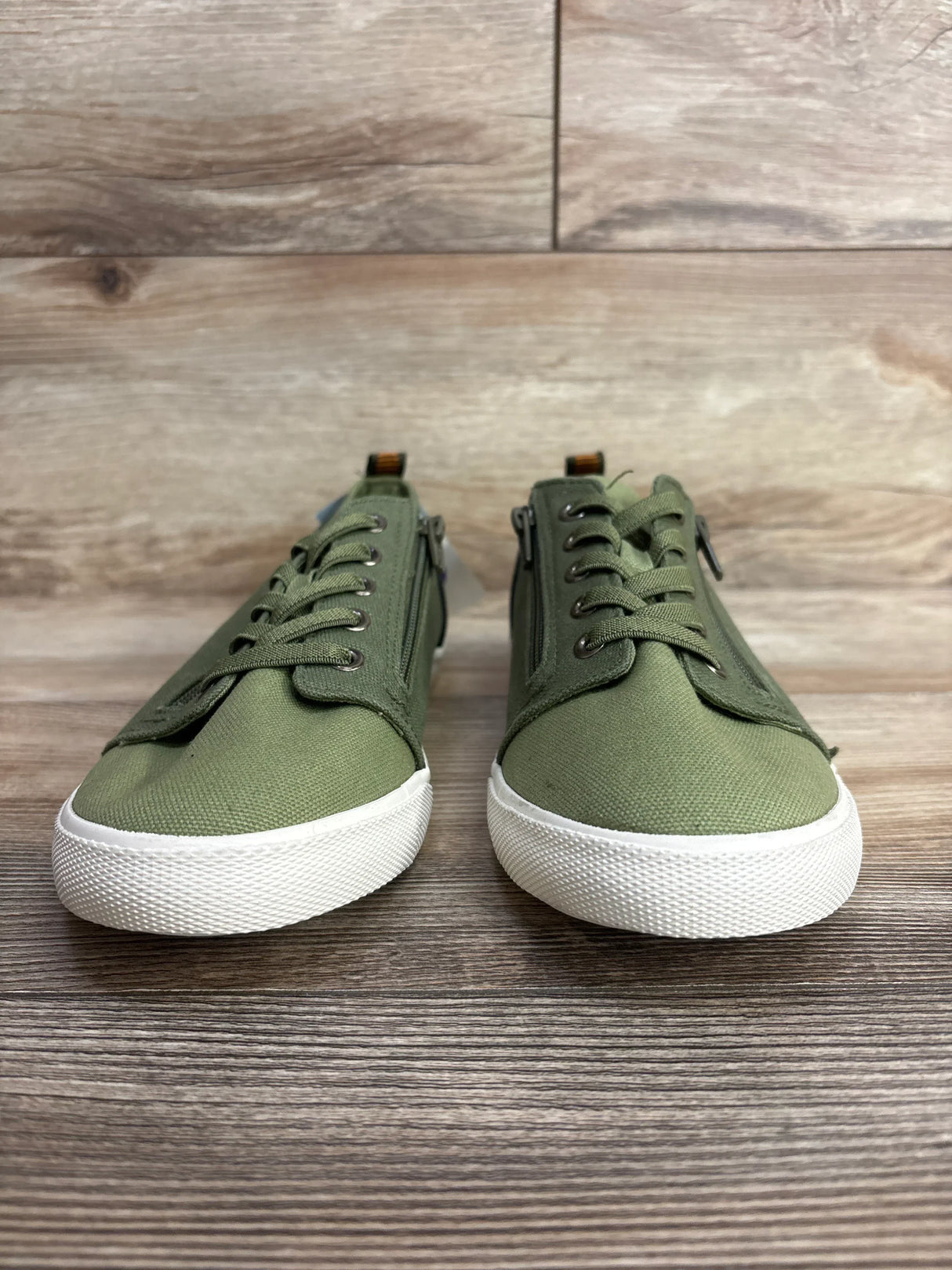 Pair of green canvas children's sneakers with white soles on wooden floor background