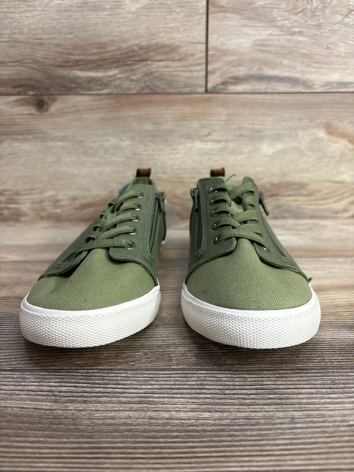 Pair of green canvas children's sneakers with white soles on wooden floor background