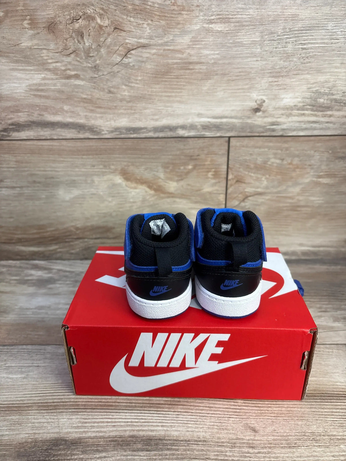 Rear view of toddler Nike Court Borough sneakers in black and game royal with Velcro on red Nike box