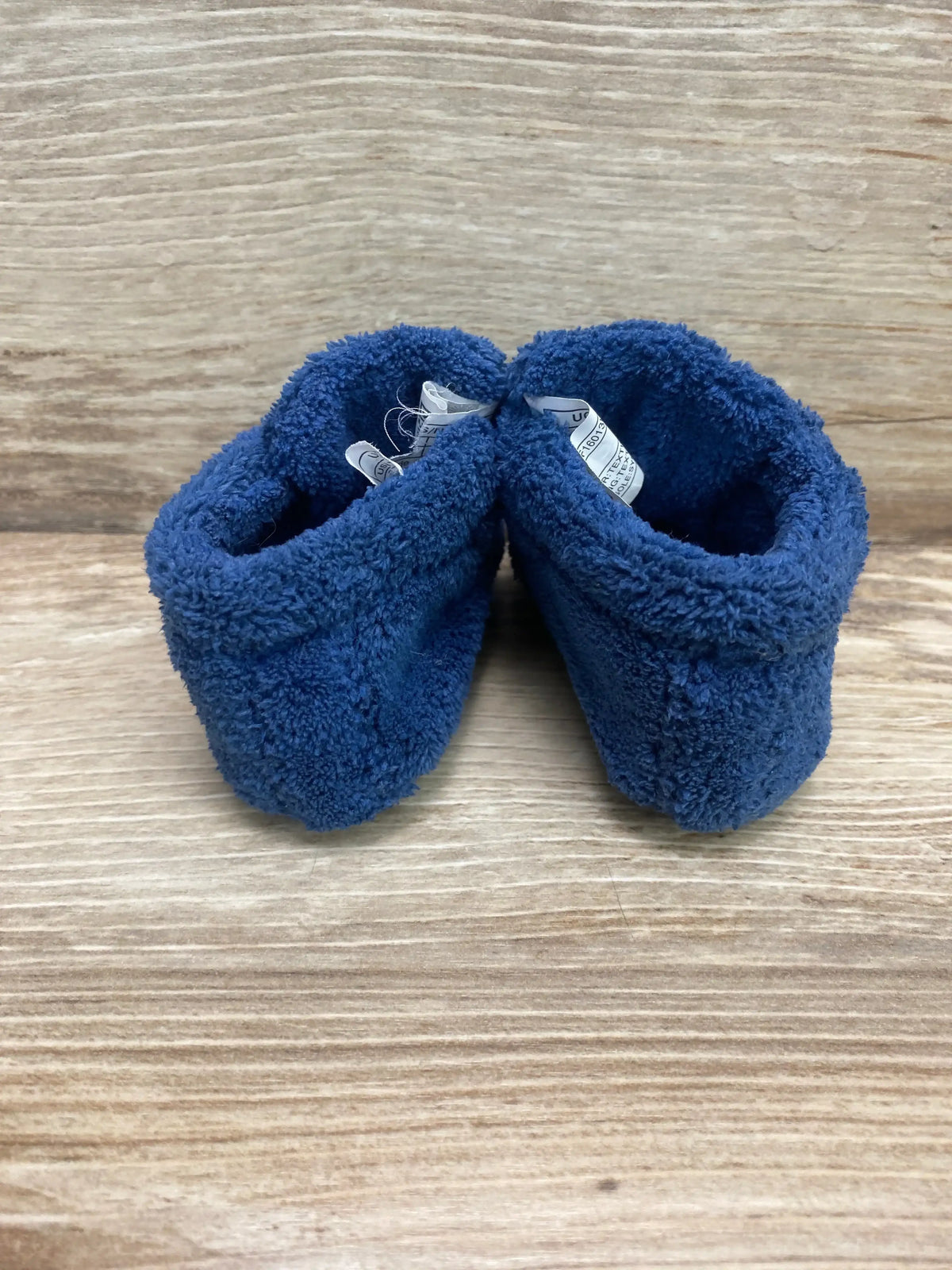 Rear view of UGG Baby Bixbee boot pair showing blue plush fleece exterior and visible plush lining on wood backdrop