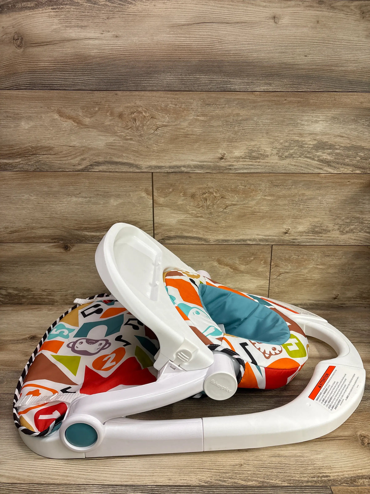 Side view of Fisher-Price Deluxe Kick & Play Sit-Me-Up Floor Seat showcasing its colorful patterned seat and white frame on a wood floor