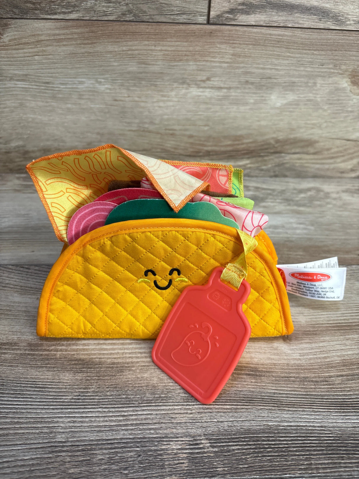 Plush taco playset with smiling face, assorted colorful fabric fillings, and toy condiment tag