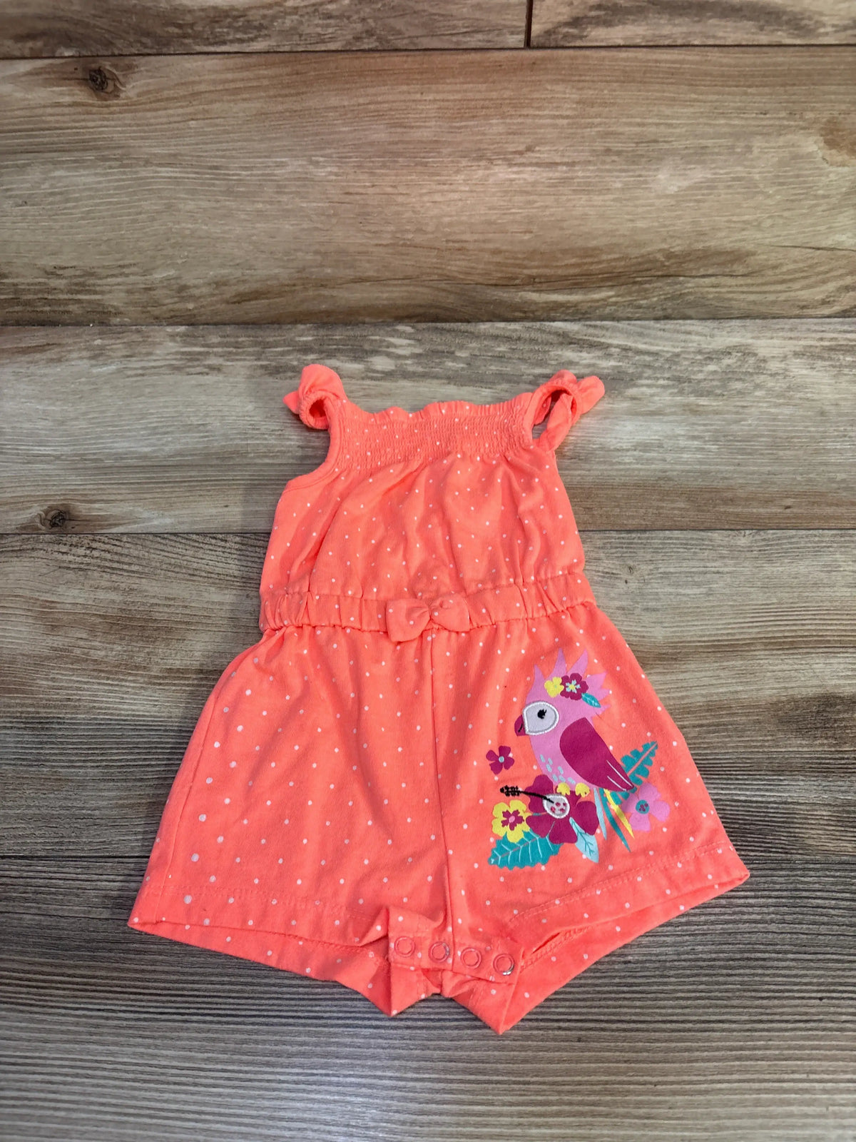 Front view of coral polka dot shortie romper showcasing bird and floral graphic on a wood background