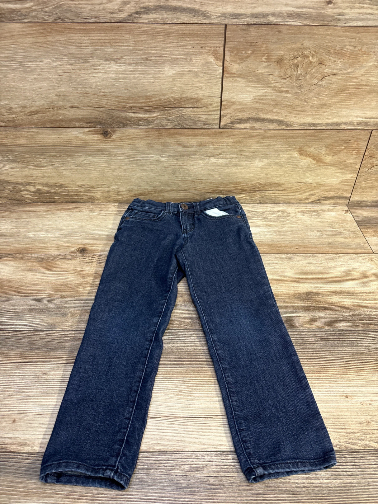Flat lay of Oshkosh toddler skinny jeans size 5T in dark blue showing narrow legs and adjustable elastic waist on wood background