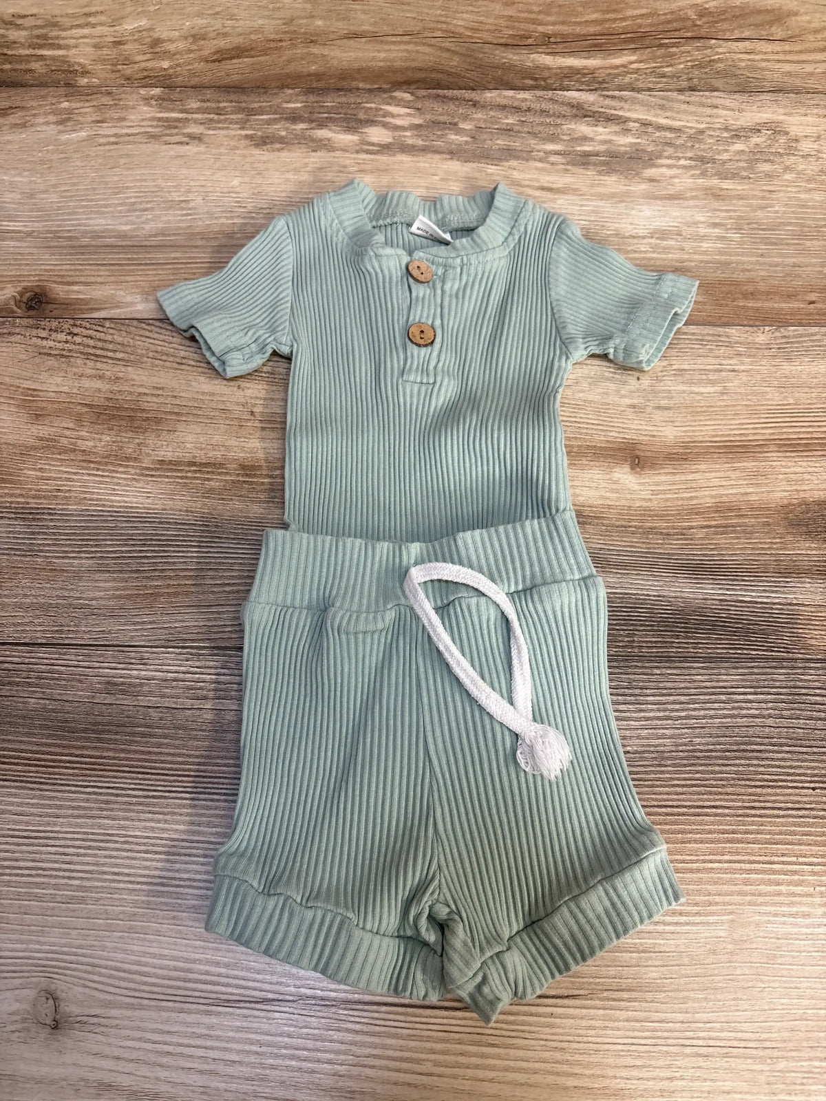 Green ribbed baby romper set with wooden buttons and shorts on wood background