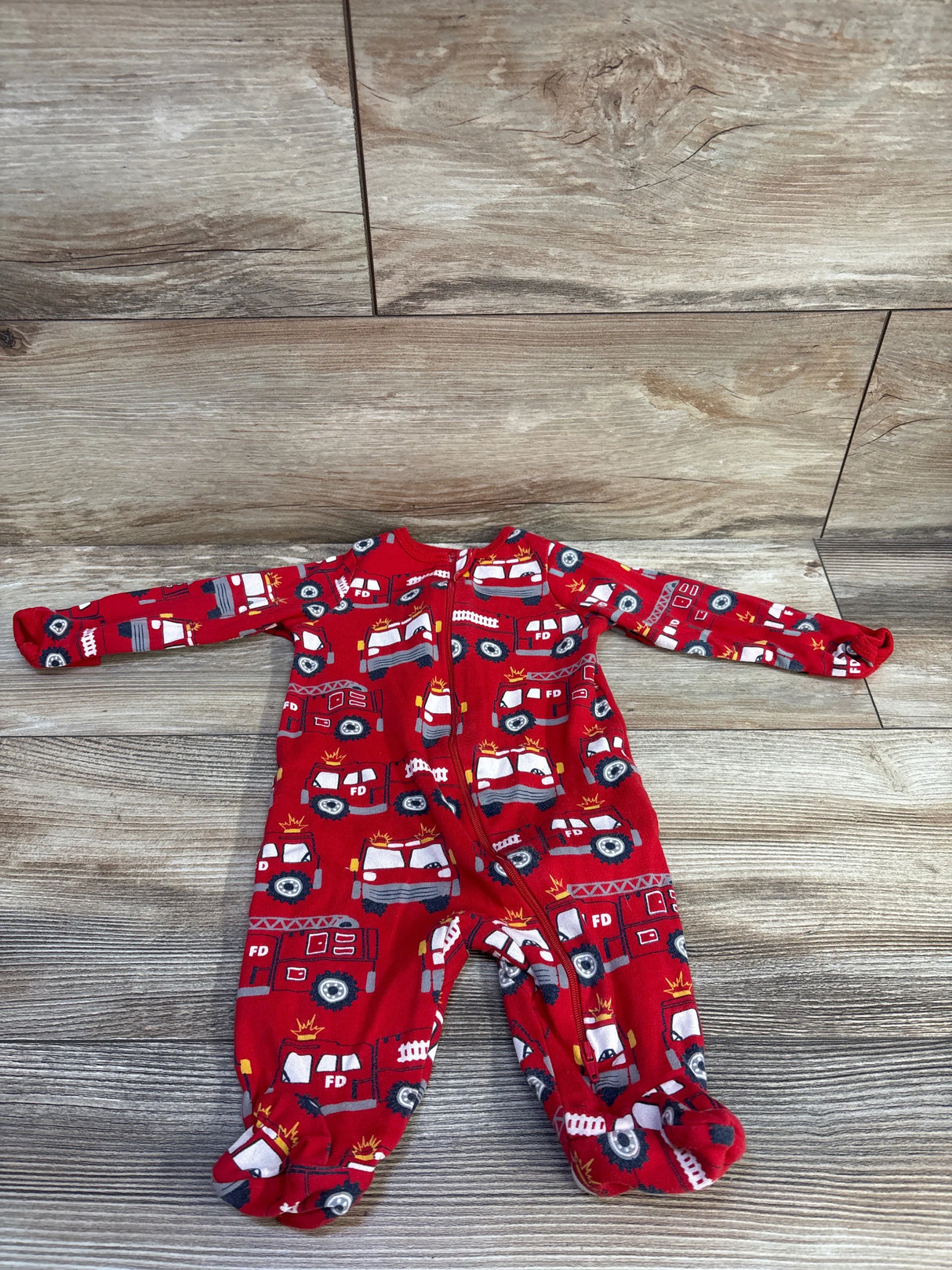 Front view of Wonder Nation red firetruck footed sleeper (0-3 months) showing all-over firetruck print and front zipper on wood floor