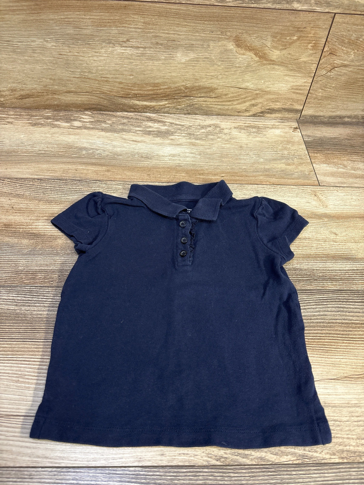 Children's Place navy blue short sleeve polo shirt for toddlers, size 3T, on a wood floor.