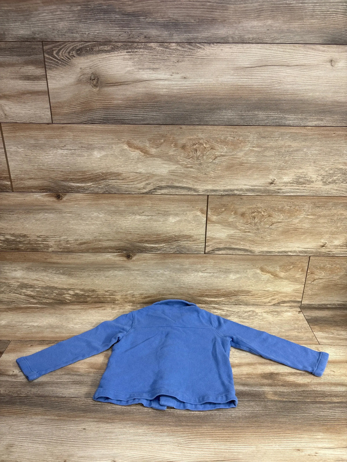 Blue long sleeve toddler shirt laid flat on wood floor background