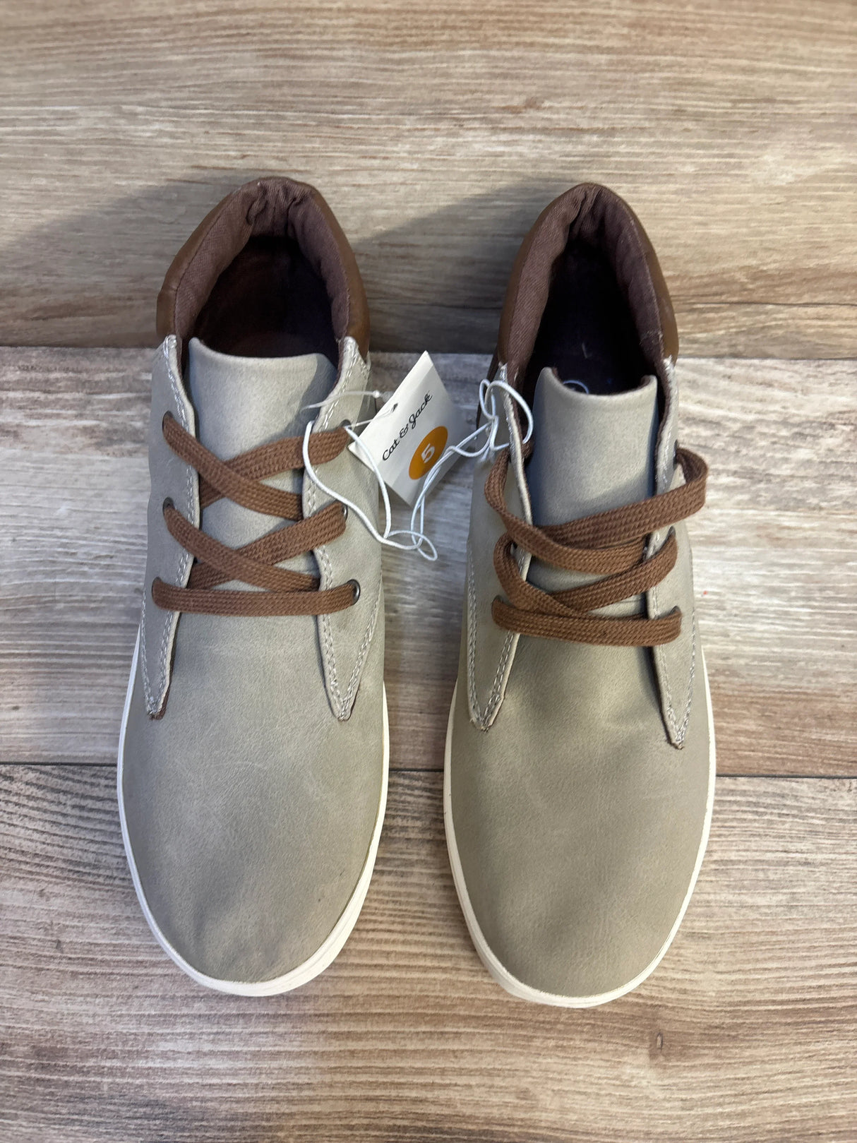Gray and brown children's lace-up shoes with tags, displayed on wooden surface