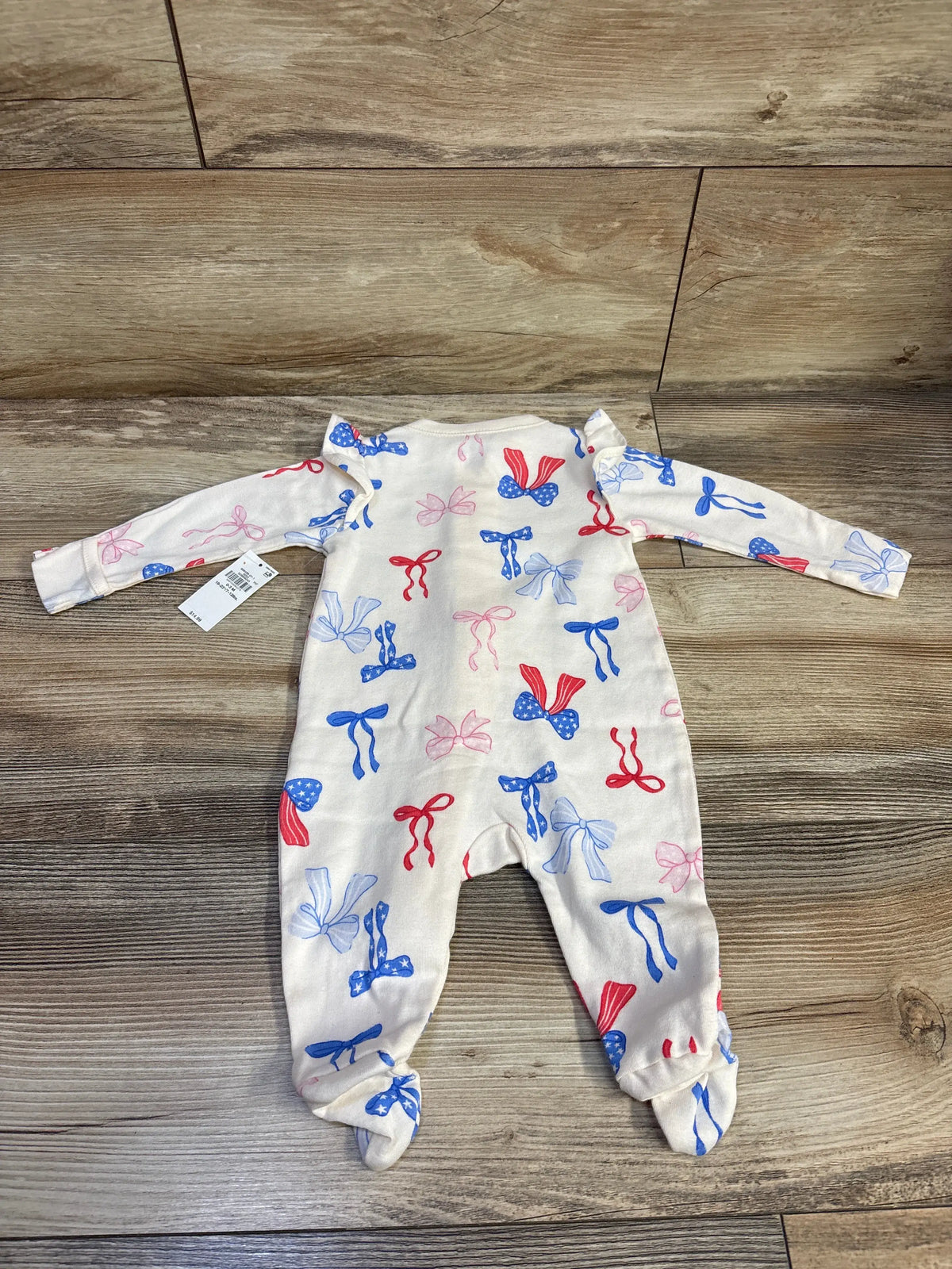 Front view of Old Navy cream cotton footed sleeper showcasing a red, blue, and white bow pattern on a wood floor