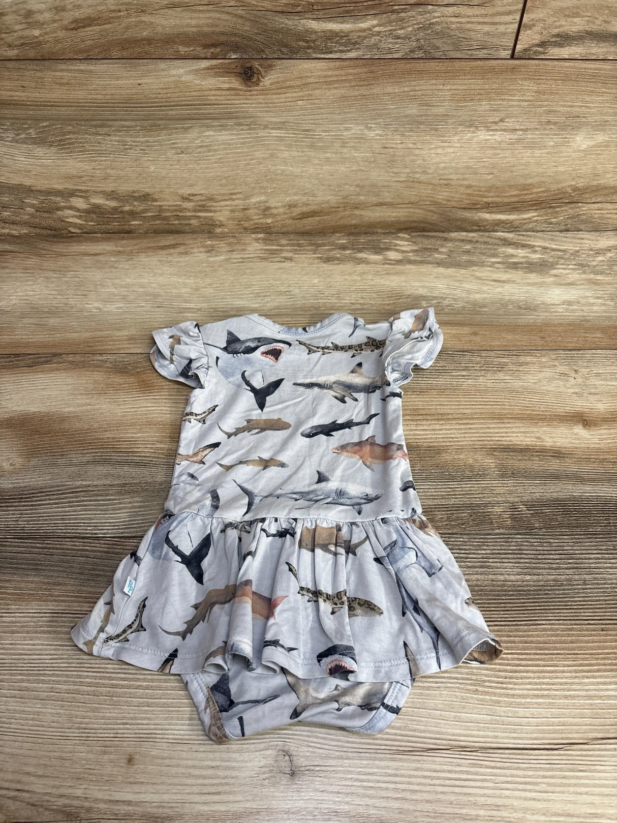Baby dress with short ruffle sleeves and shark print pattern laid flat on wooden surface