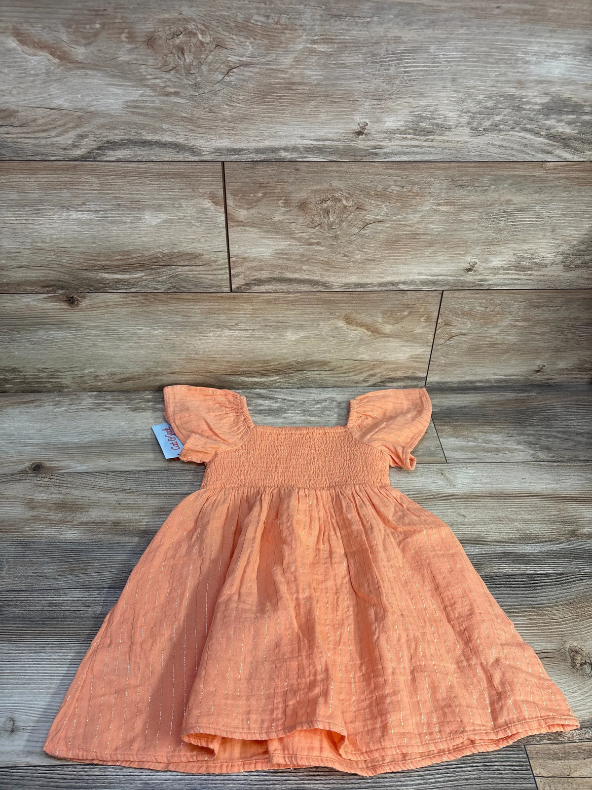 Front view of Cat & Jack 4T peach orange short sleeve dress showcasing gold stripes and smocked bodice on wood flooring
