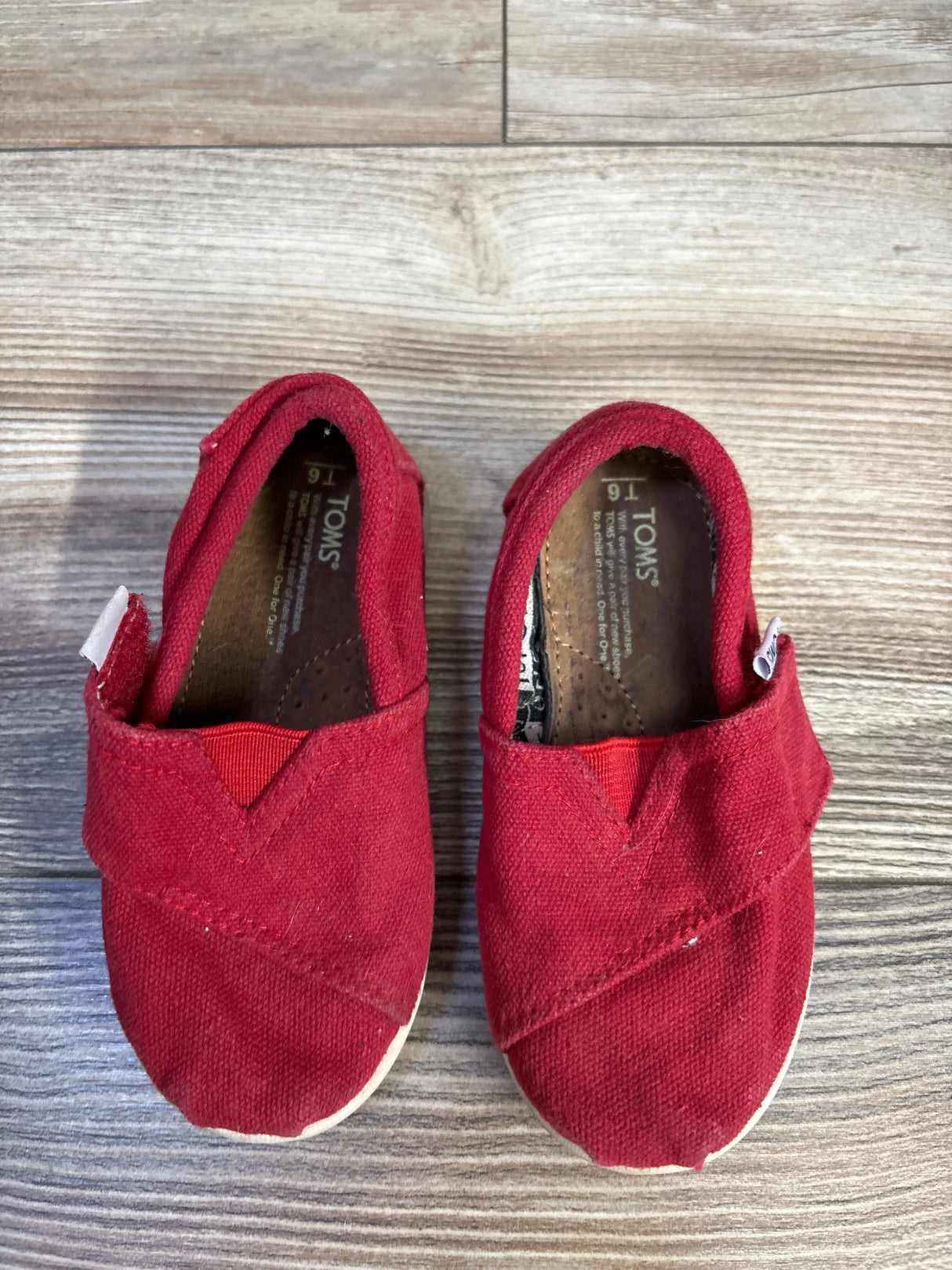 Pair of toddler red TOMS slip-on shoes size 16 on wooden floor for kids resale