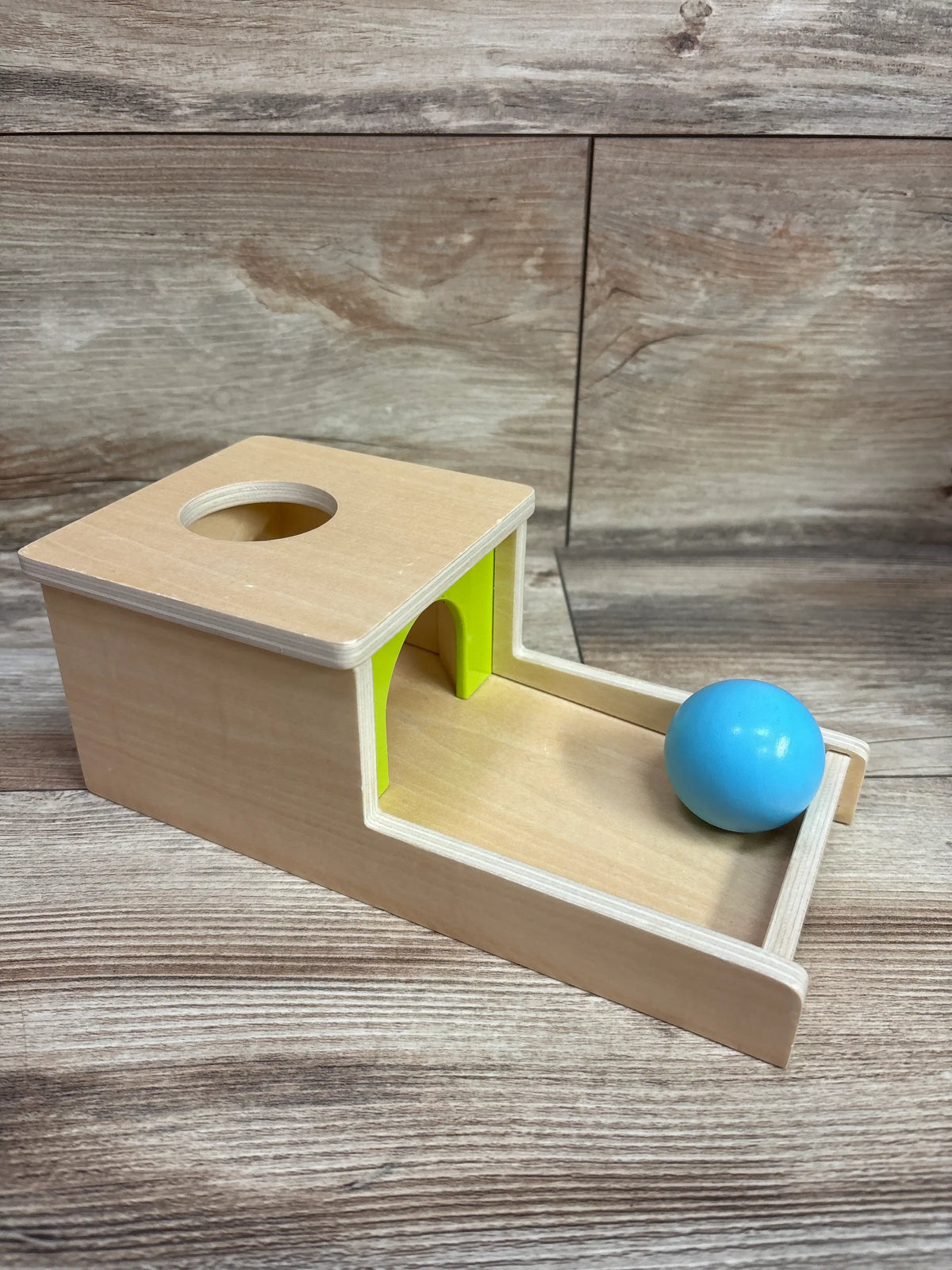 Angled view of Adena Montessori Wooden Object Permanence Box showcasing blue ball and open track against wood grain background