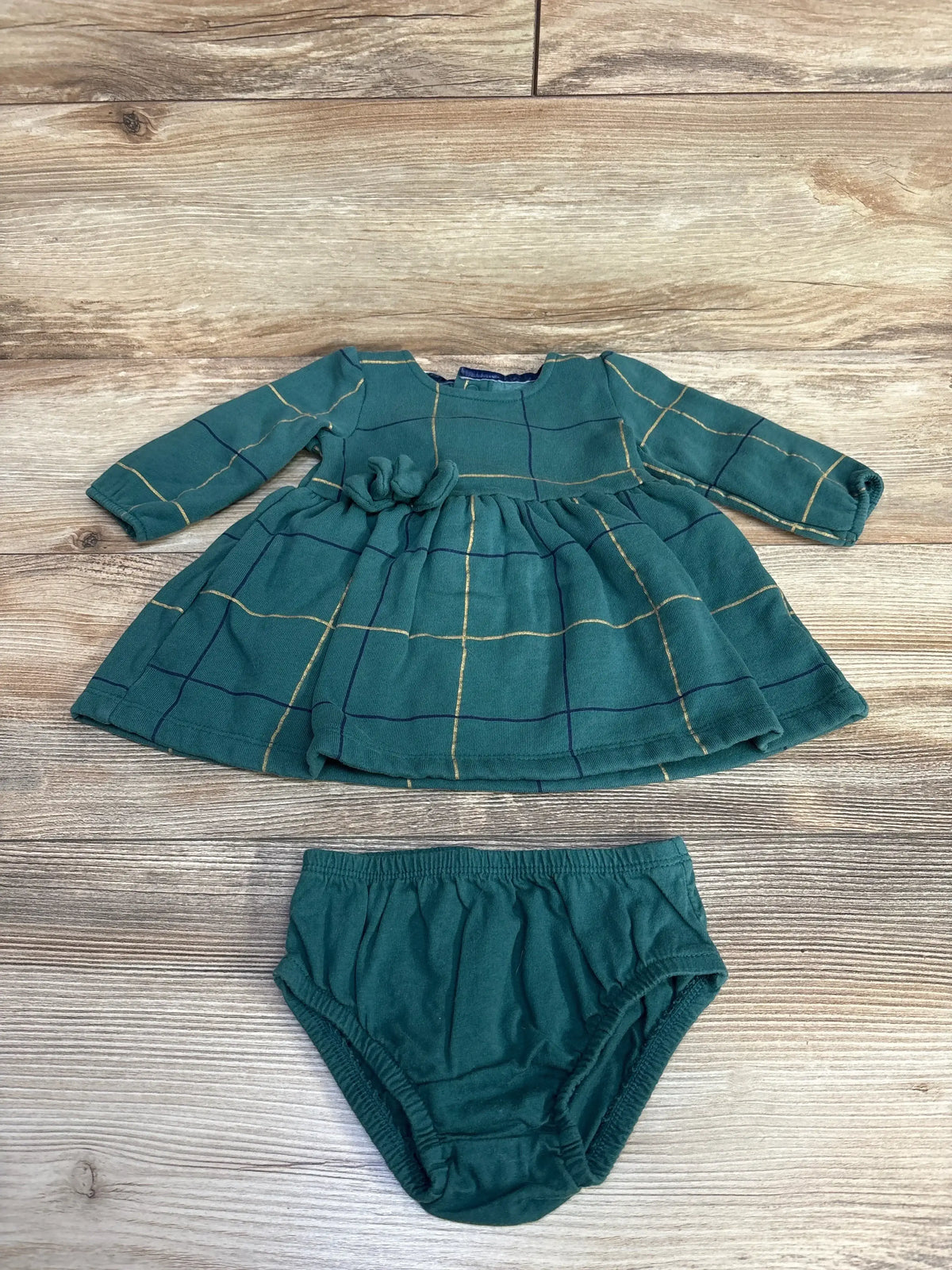 Green baby dress with long sleeves and floral detail, paired with matching green bloomers on wood background