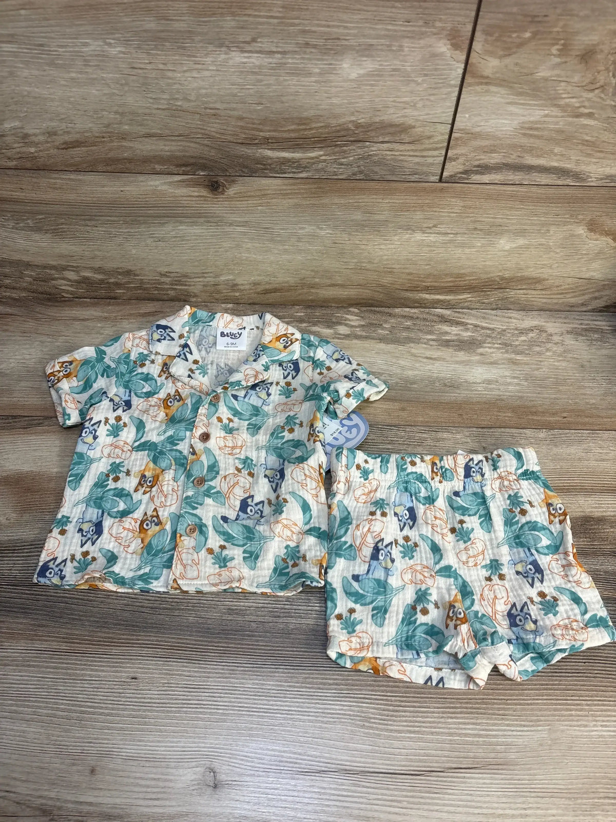 Baby short-sleeve shirt and shorts set with blue and orange animal print, laid on wood floor