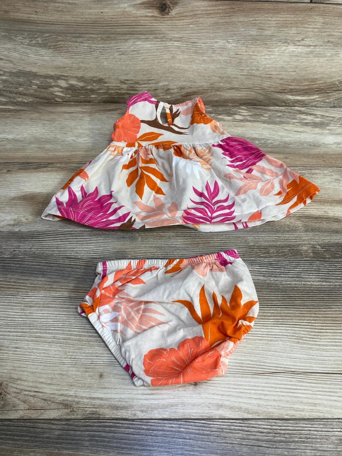 Top-down view of Carter’s 2-piece dress and bloomers showcasing orange and pink tropical leaf print on light wood background
