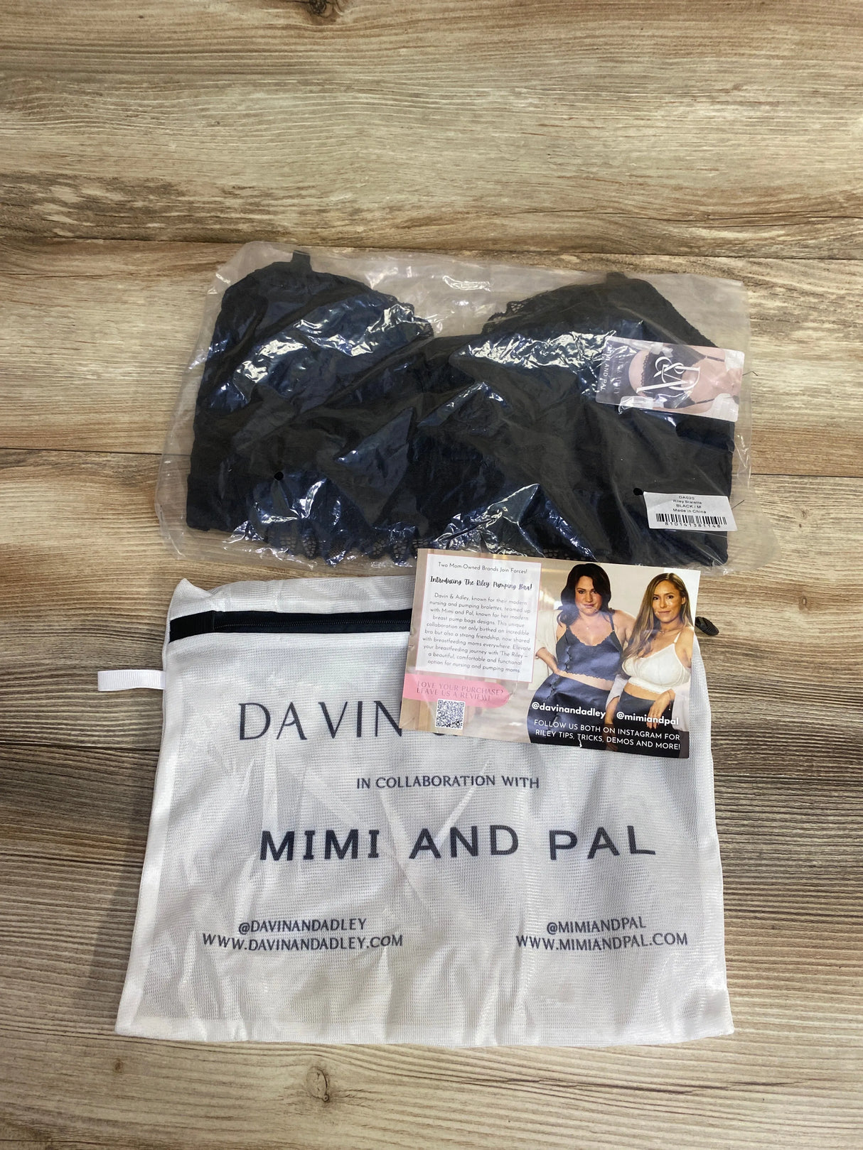 Black nursing and pumping bra in clear packaging with white Davin and Adley cloth bag, promotional card on wood surface