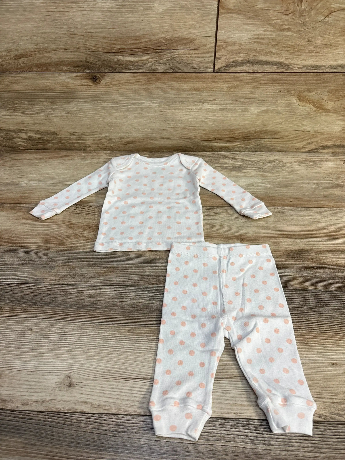 Flat lay of white 2-piece pajama set with pink polka dots showing long-sleeve top and cuffed pants on wood background