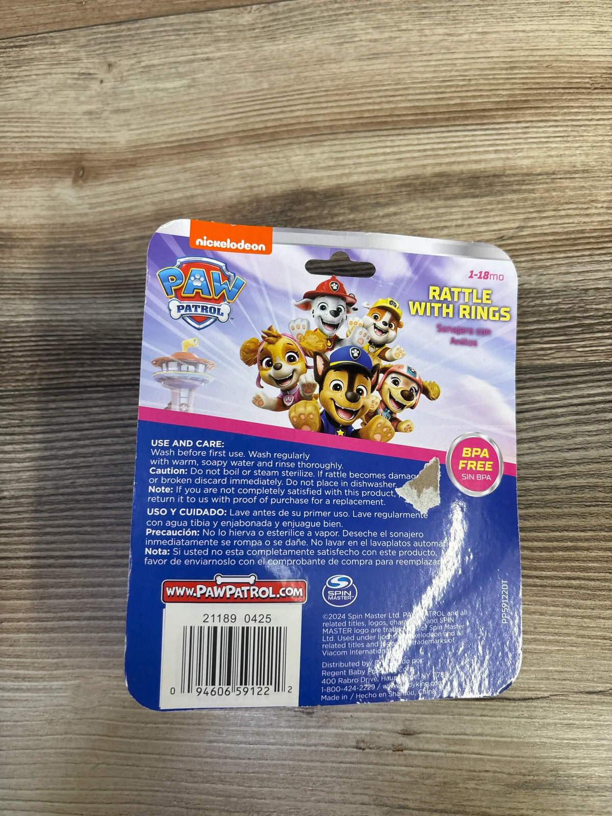 Back view of Nickelodeon PAW Patrol rattle packaging showcasing the Rattle with Rings headline and BPA free badge on a wood table