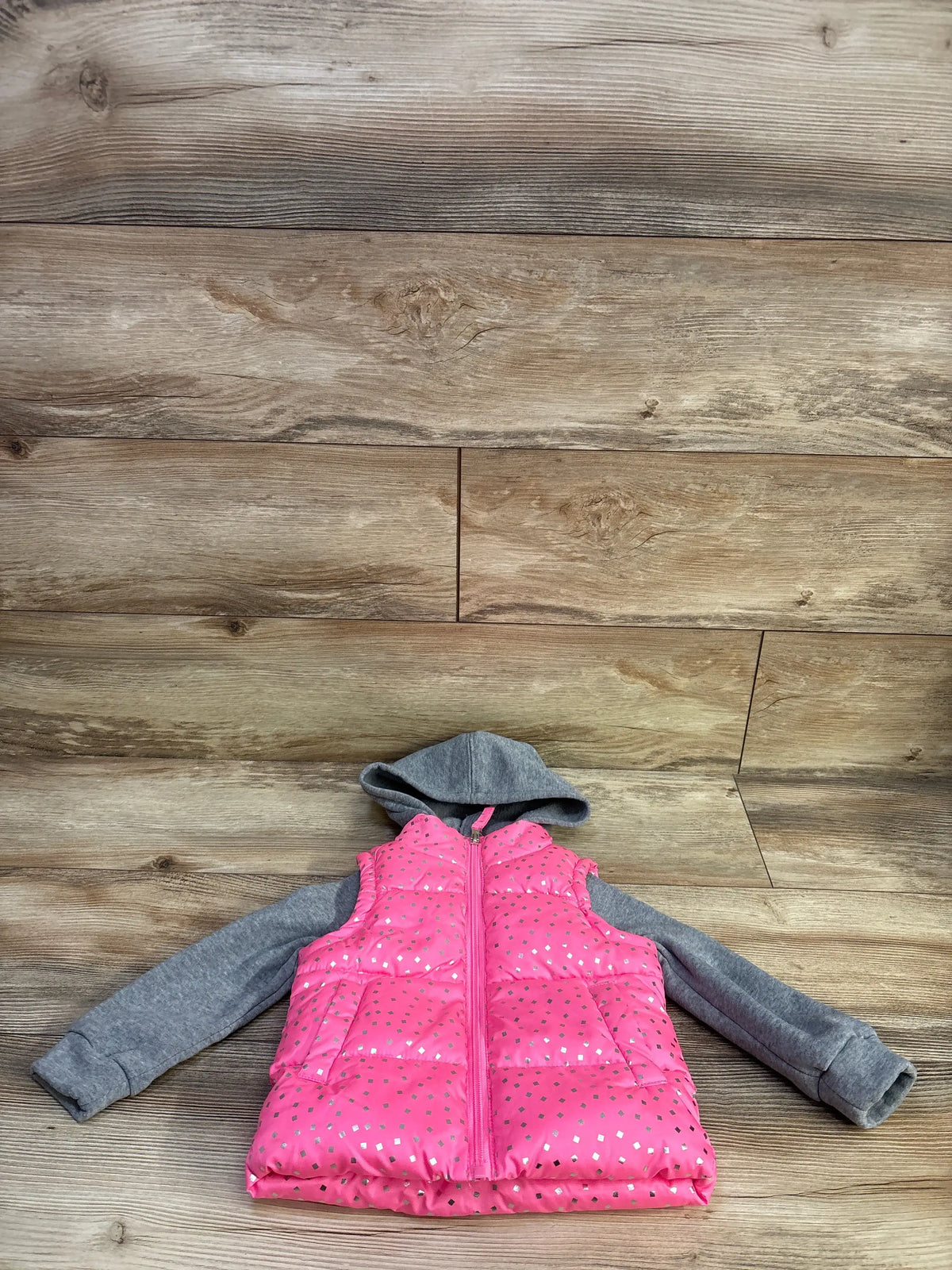 Flat lay of toddler pink 2fer puffer jacket with silver foil squares, gray hood and sleeves, front zipper and pockets on wood background