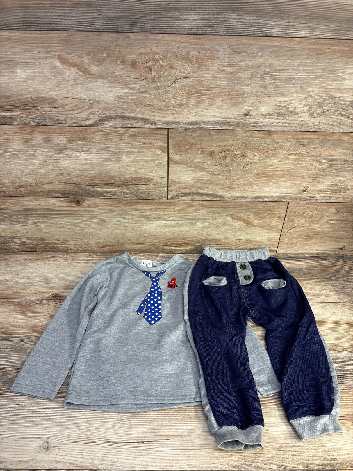 Children's gray long sleeve shirt with blue polka dot tie and blue pants with pockets on wooden floor