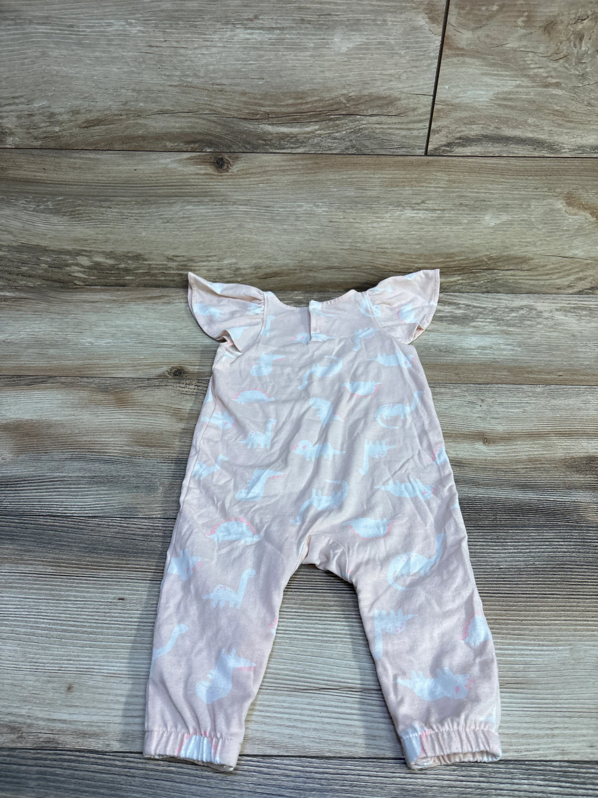 Flat lay of Cat & Jack pink dinosaur jumpsuit showcasing flutter sleeves and elasticized ankles on wood floor