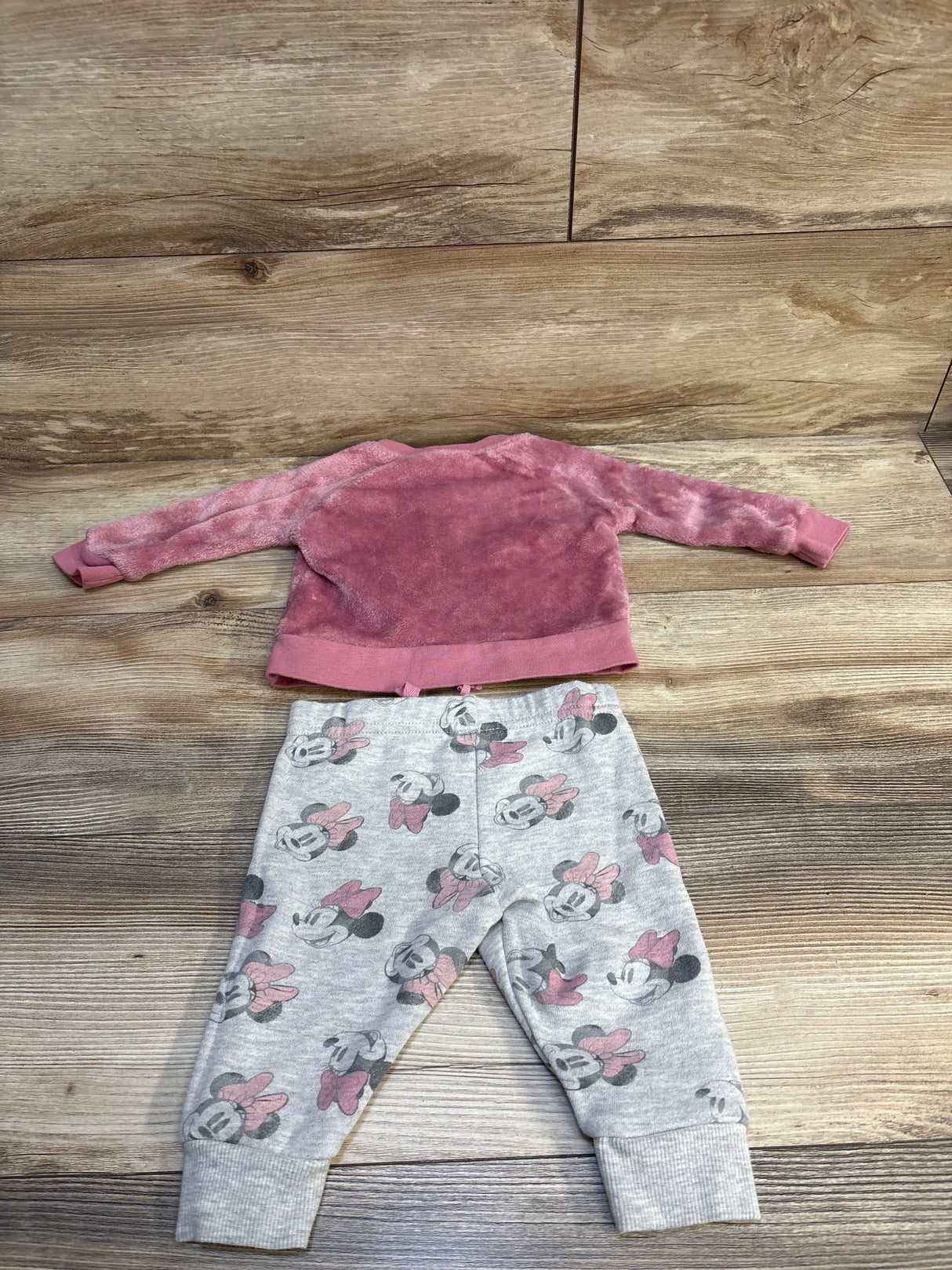 Pink fuzzy long-sleeve toddler shirt with gray Minnie Mouse print pants on wood floor