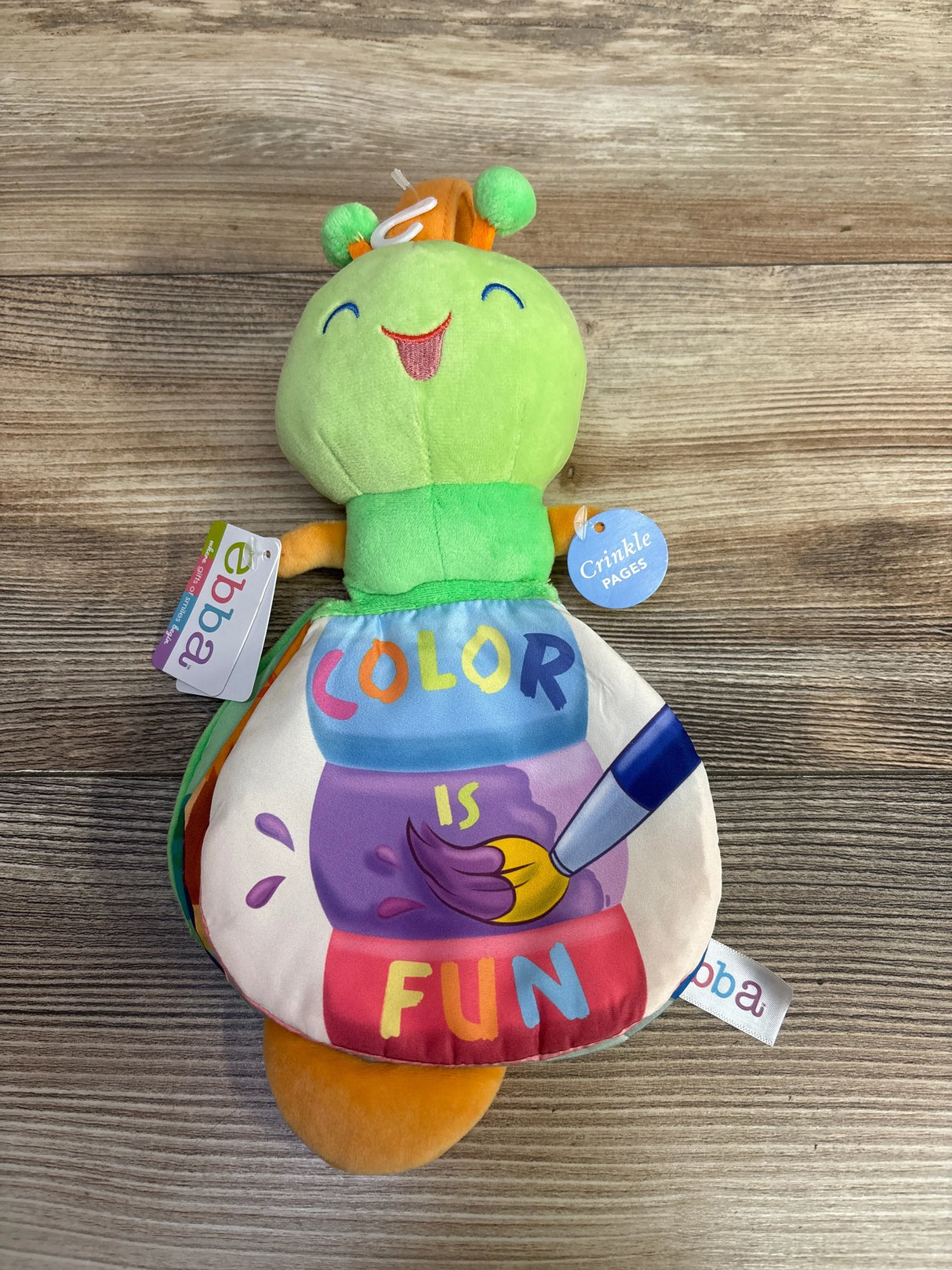Colorful plush caterpillar baby toy with 'Color is Fun' and crinkle pages on wood surface