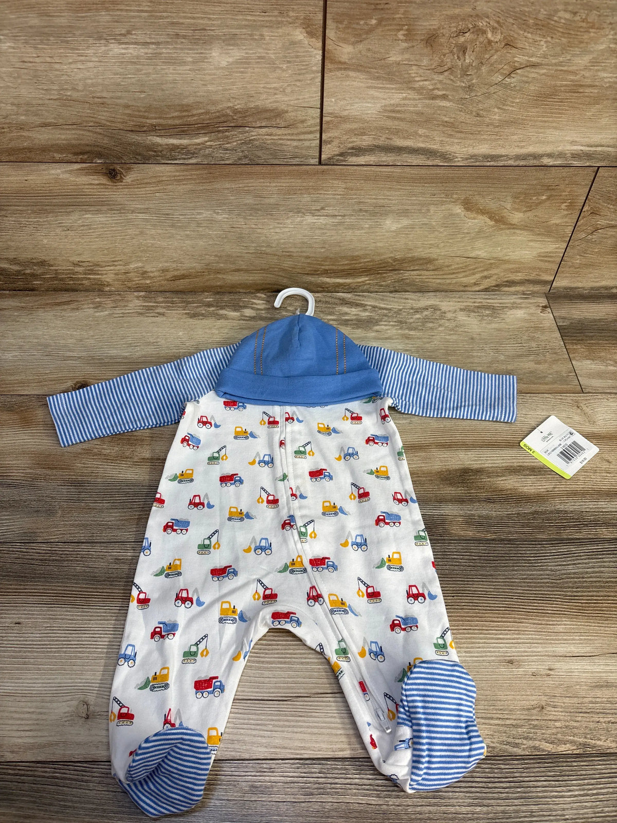 Front view of Little Me 2-piece sleeper and hat set showcasing construction vehicle print and blue striped accents on a wood surface