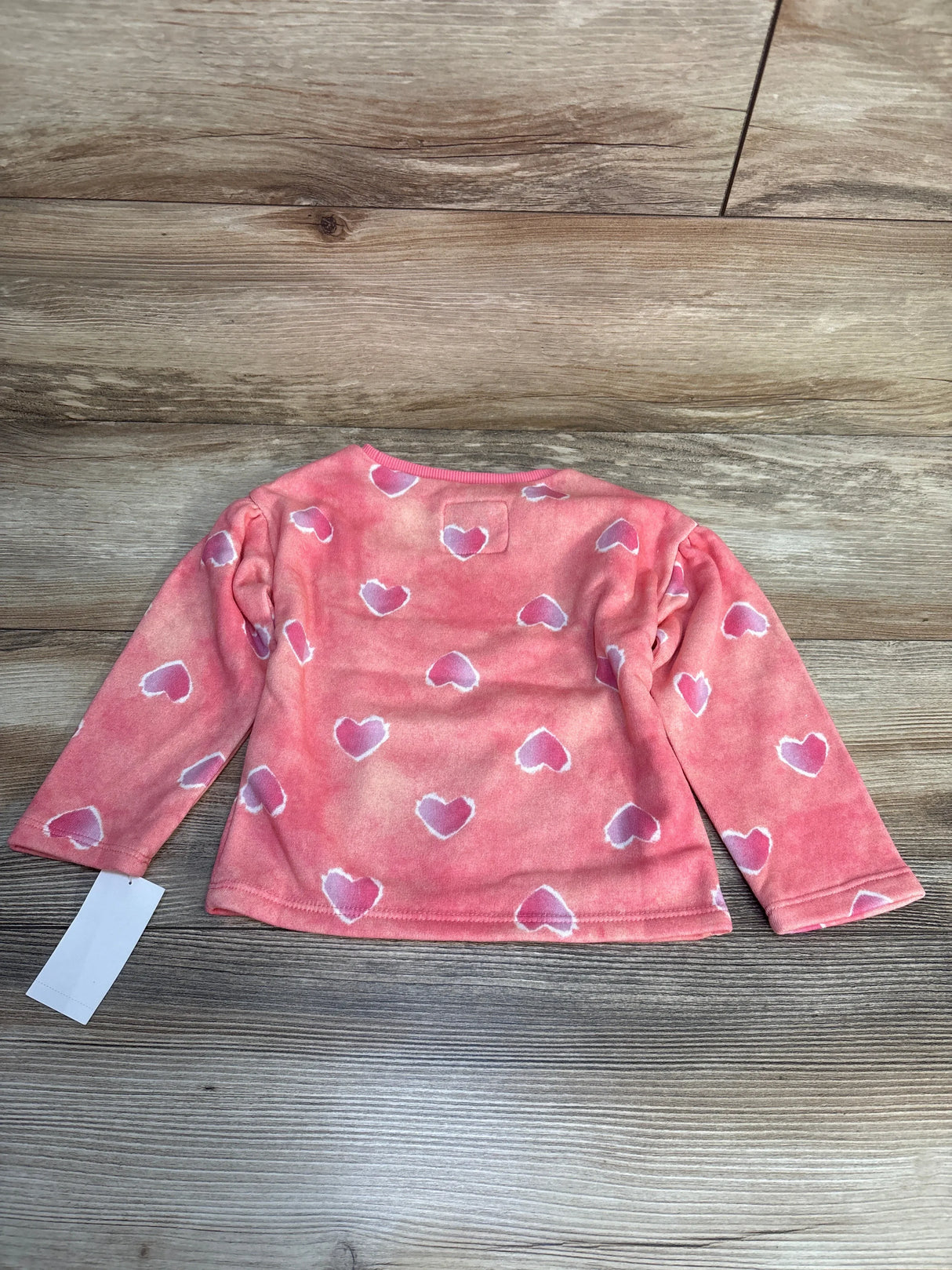 Pink long sleeve toddler shirt with white heart pattern on wooden floor
