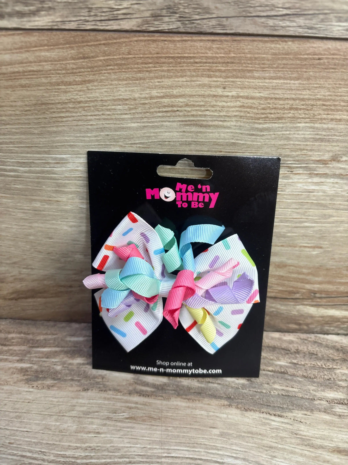 Front view of NEW Birthday Hair Bow White showcasing sprinkle print with pastel curly ribbons on branded card and wood plank background