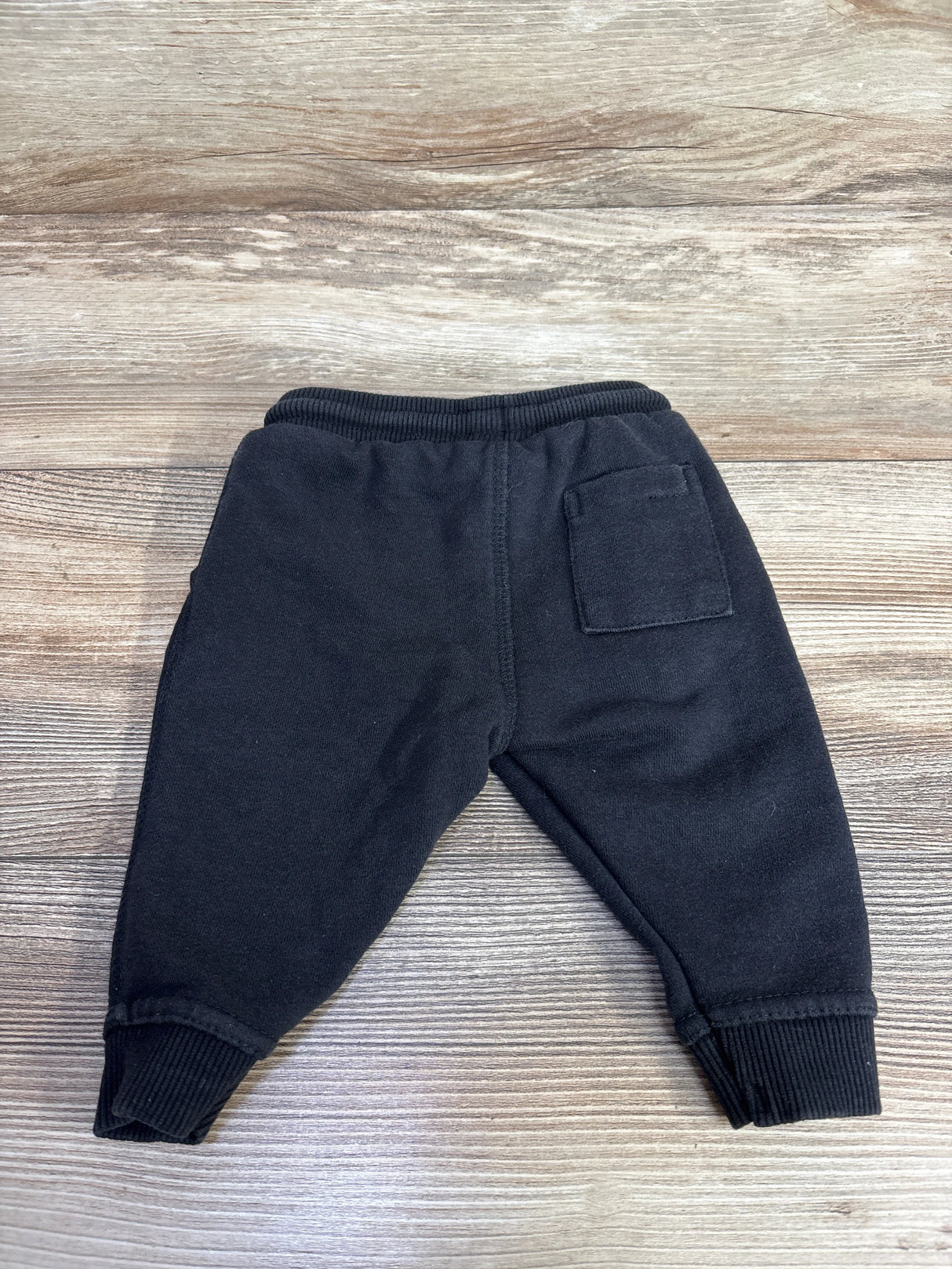 Back view of black toddler sweatpants with ribbed cuffs and one back pocket on wood background