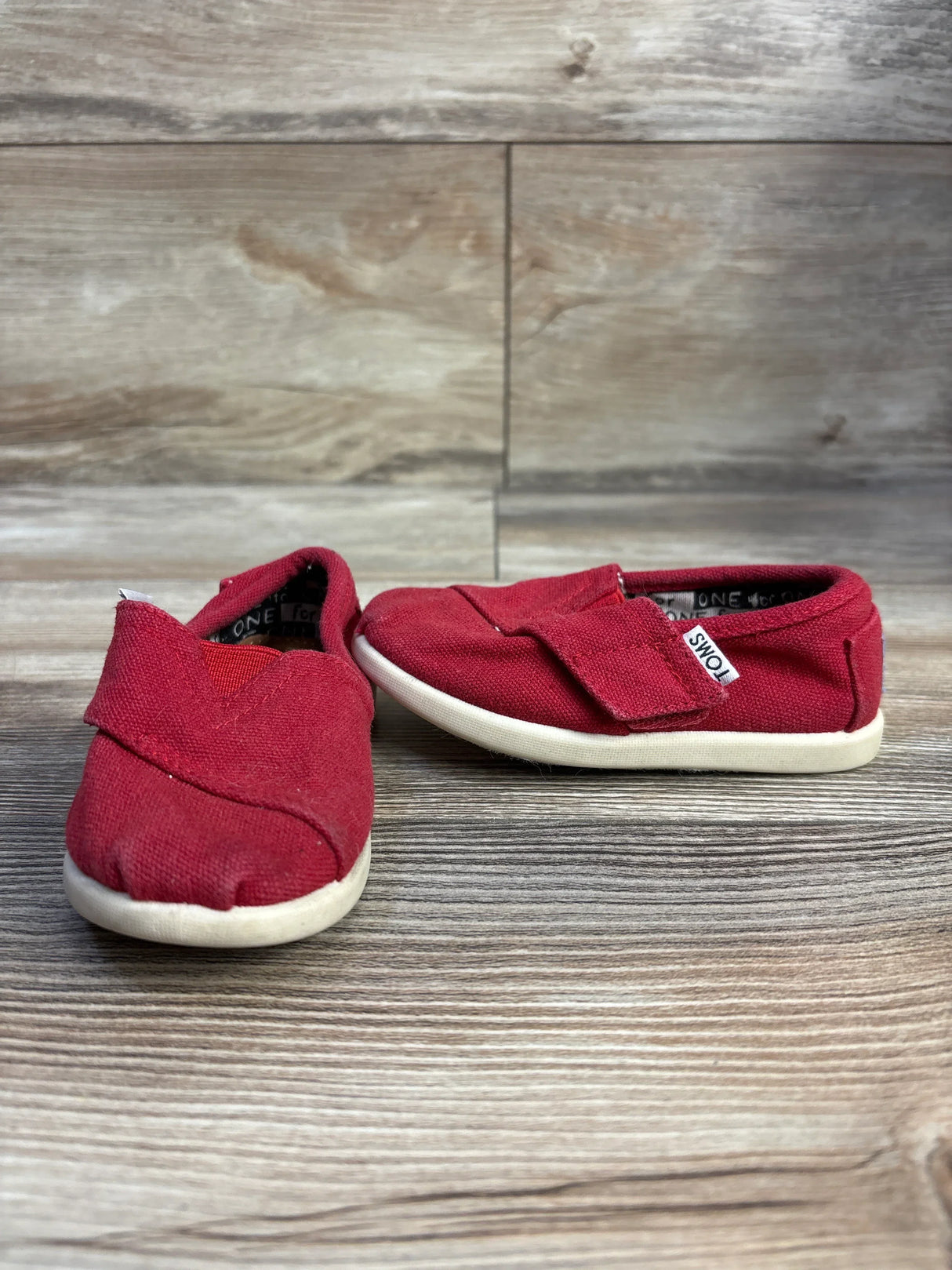 Pair of red toddler TOMS canvas shoes with white soles on wooden floor backdrop