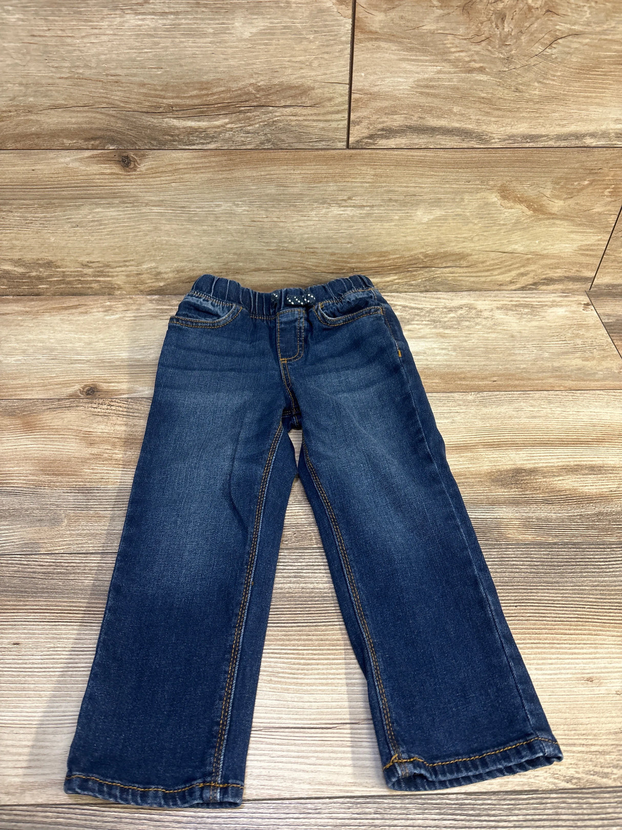Flat lay of Jumping Beans toddler jeans showcasing elastic drawstring waist, blue denim, size 3T on wood background