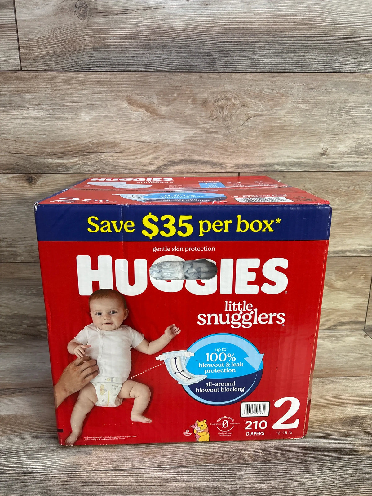 Front view of Huggies Little Snugglers Size 2 diaper box showing 210 diapers and blowout and leak protection on wood flooring