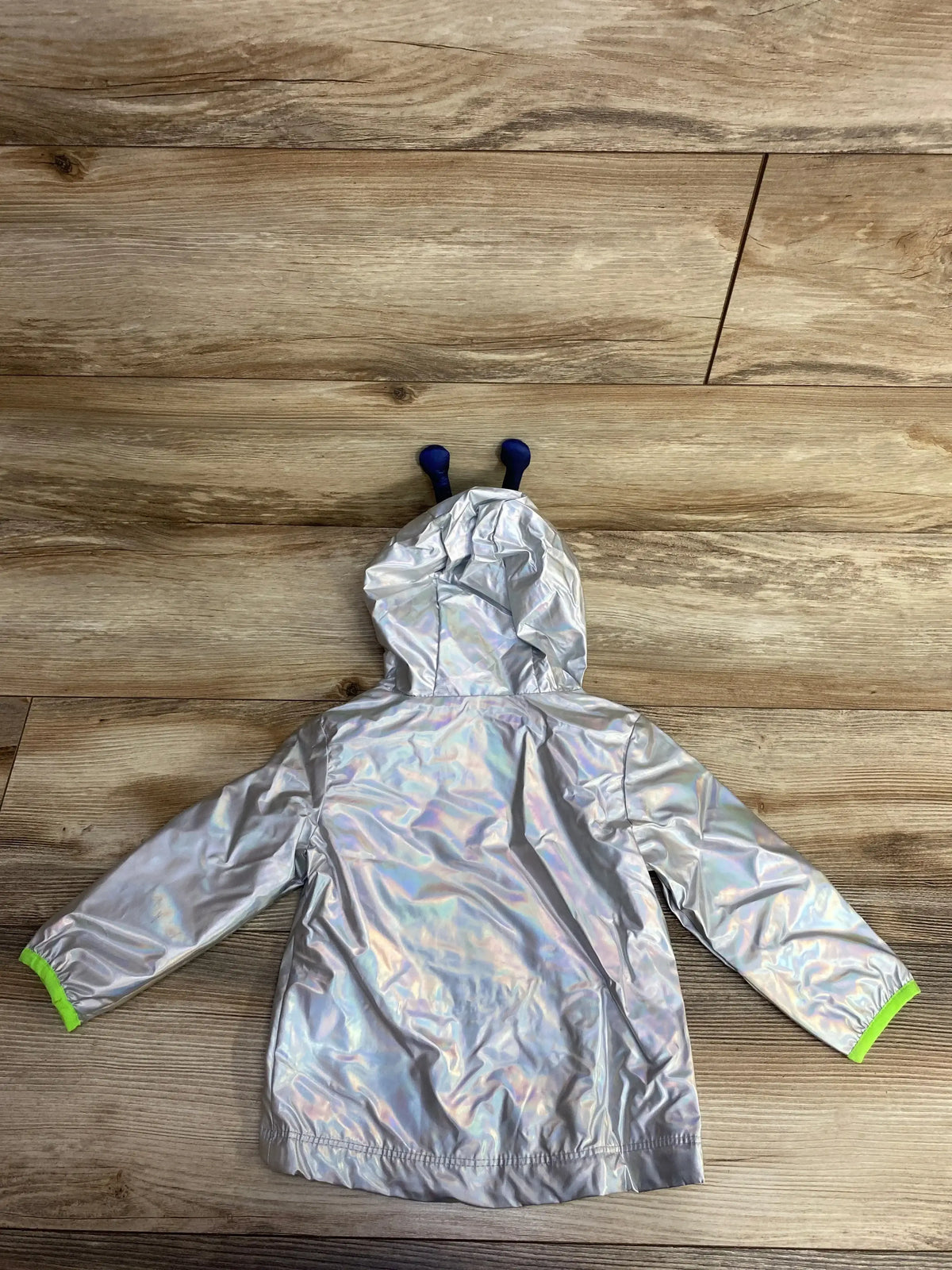 Back view of Cat and Jack holographic toddler rain jacket (12M) showing iridescent silver fabric, blue hood antennae and green cuffs on wood floor