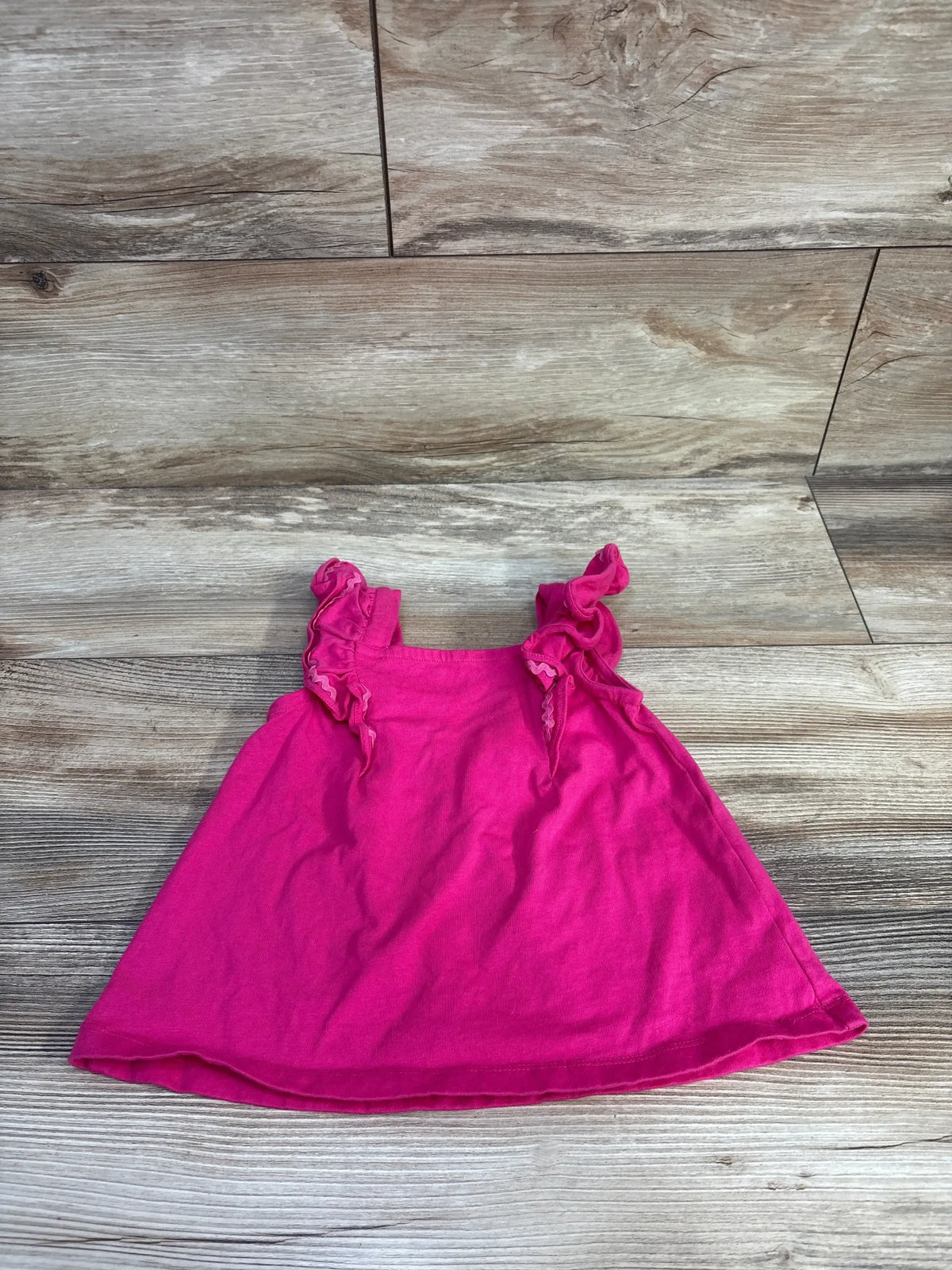 Flat-lay of hot pink Janie & Jack toddler ruffle-strap jersey top showing ruffled shoulder straps on wood floor