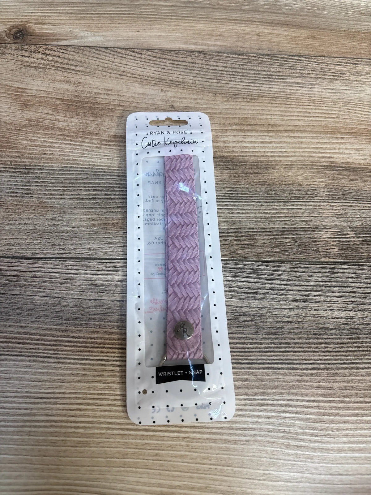 Pink braided wristlet keychain in retail packaging on wooden surface