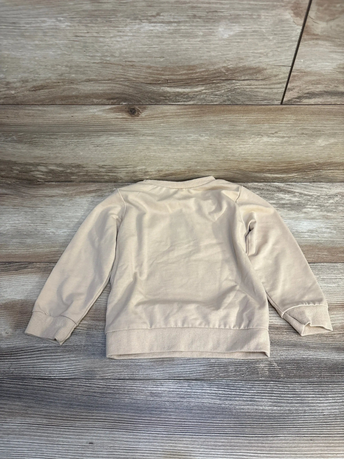 Beige long sleeve kids sweatshirt laid flat on wood background, children's clothing resale