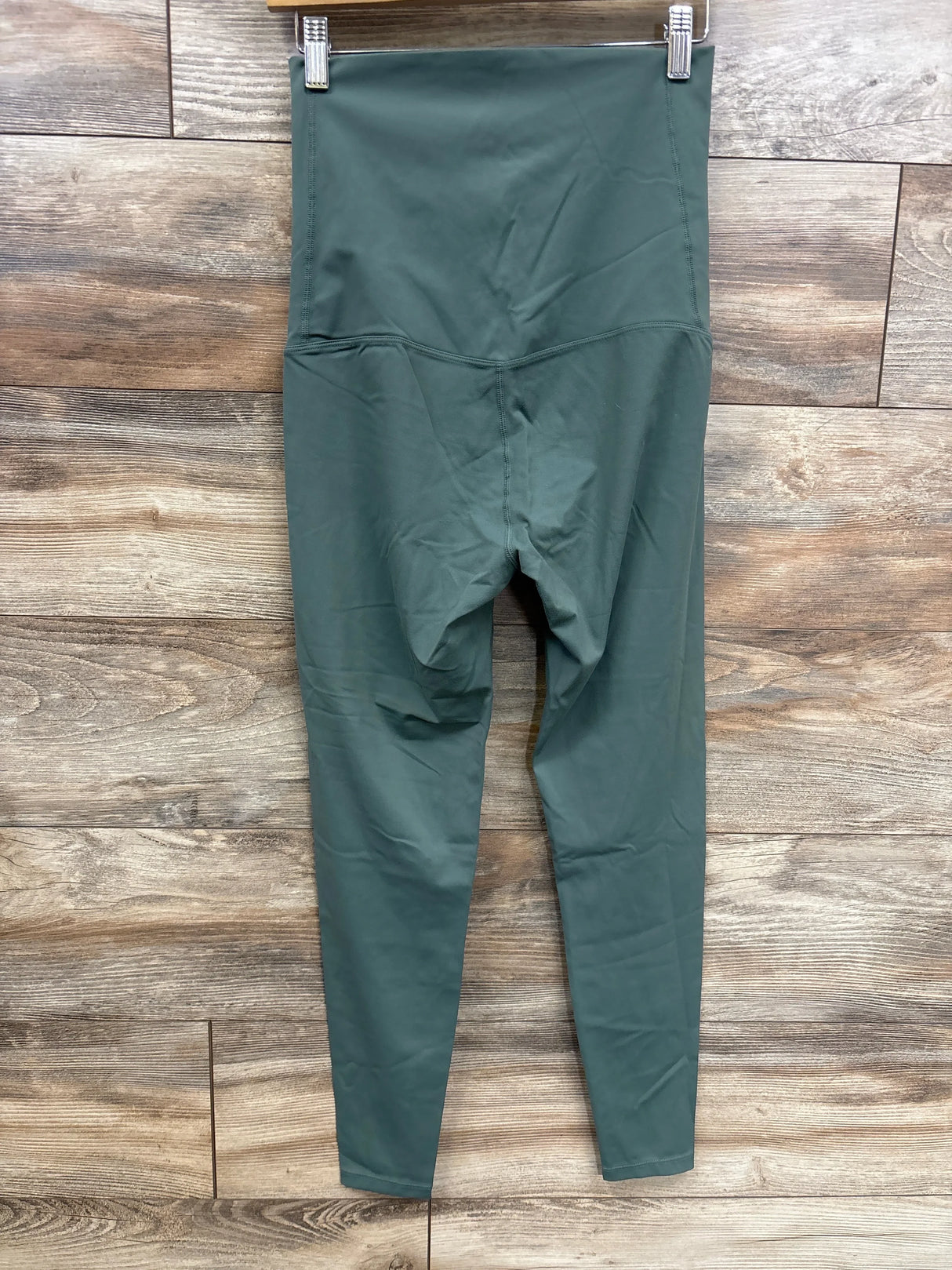 Front view of olive maternity leggings with high full-panel waistband and full-length legs on wood plank background