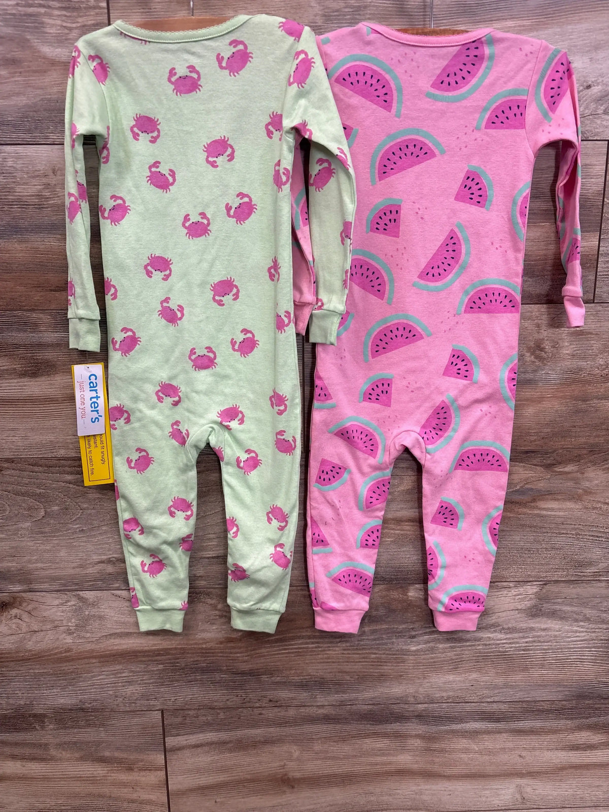 Two long sleeve kids pajamas, one green with pink crabs, one pink with watermelon print.