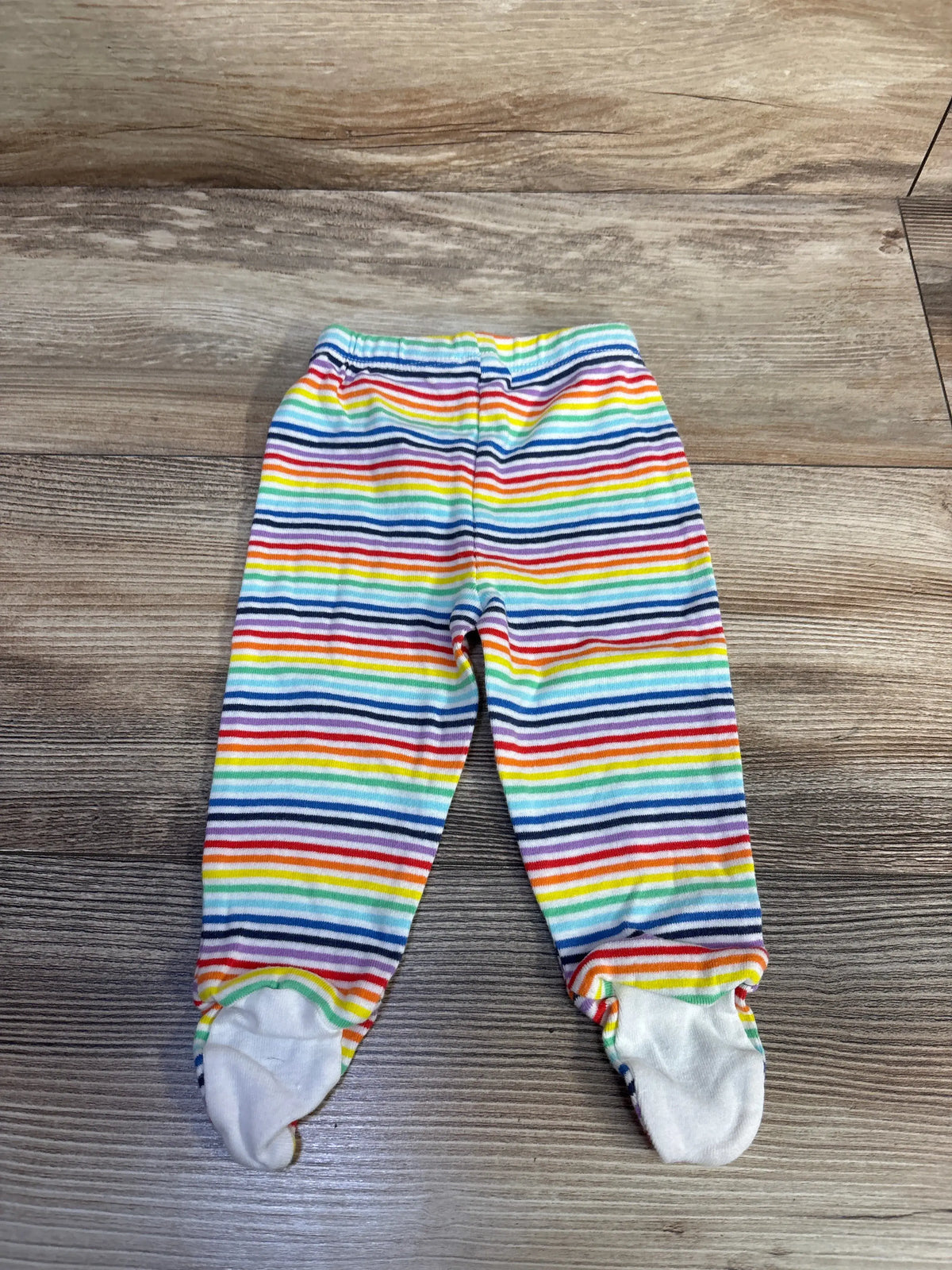 Front view of Primary striped footed pants showcasing rainbow stripes and covered feet on a wood-grain surface